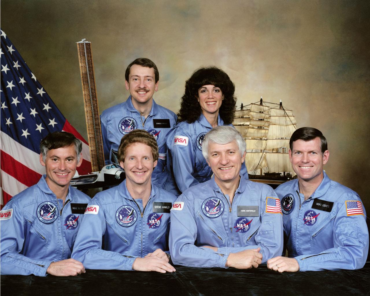 S84-30259 (April 1984) --- NASA's Discovery will carry these six STS51-D crew members into space on an early summer mission. Astronaut Henry W. Hartsfield Jr. (second right, front row) is crew commander; and Michael L. Coats, right, is pilot. Astronauts Richard M. (Mike) Mullane, left; Steven A. Hawley (second left) and Judith A. Resnik are mission specialists. Charles D. Walker (back row) is payload specialist. Both the early ocean-going Discovery and the debuting spacecraft are depicted in the backdrop. The conspicuous payload in the cargo bay of the spacecraft is that of NASA's Office of Aeronautics and Space Technology (OAST-1). Photo credit: NASA