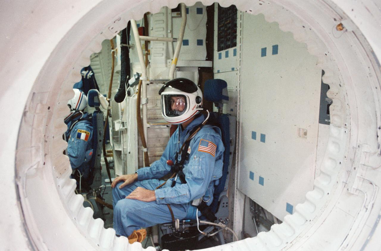 STS 51-E crew is briefed on the Shuttle full fuselage trainer. View of the crewmembers seated at stations inside the cabin was taken from the side hatch.