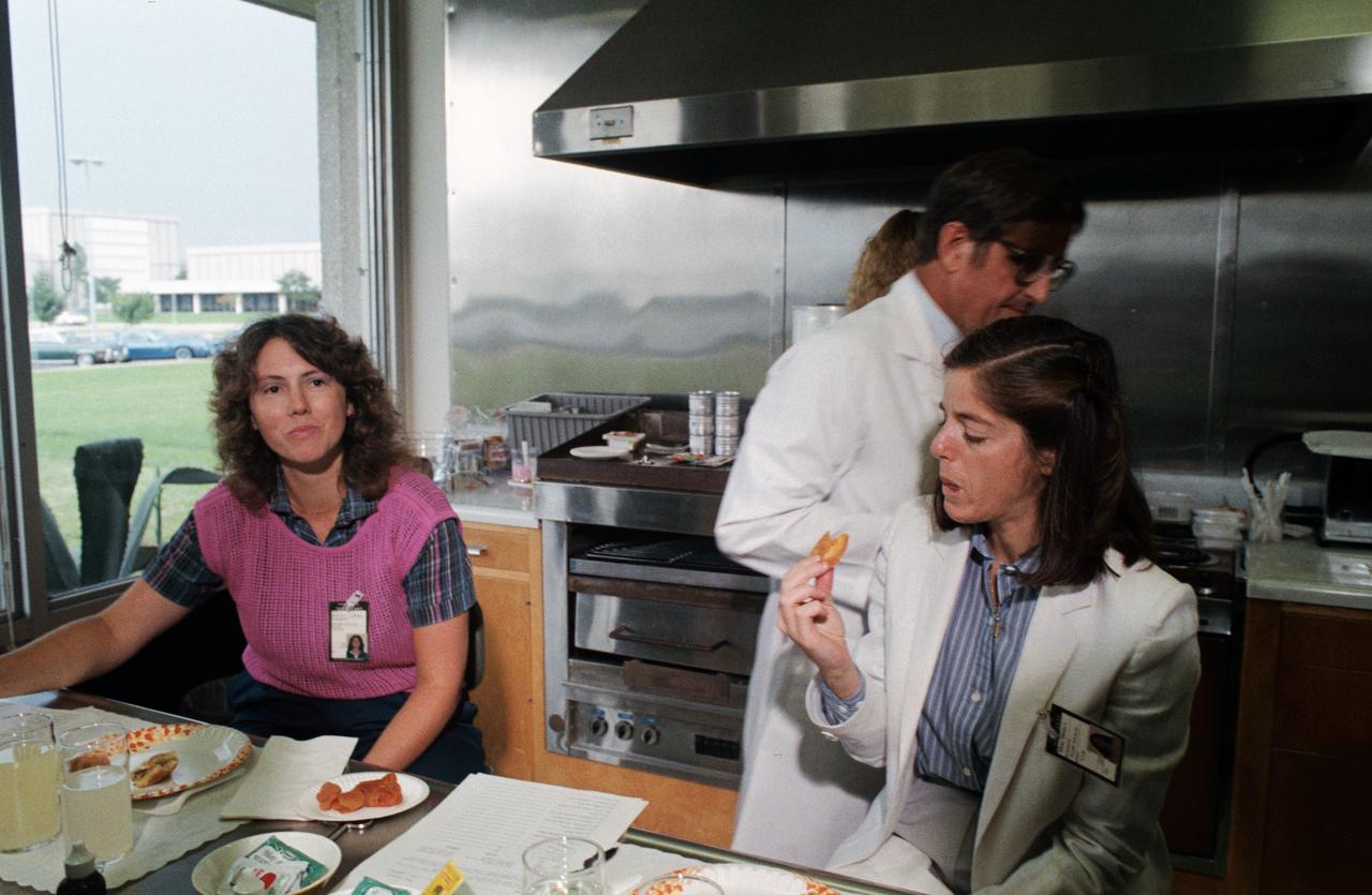 S85-39978 (10 Sept. 1985) --- Sharon Christa McAuliffe, left, appears to be deciding what she thinks of a piece of space food she tastes during a session of interfacing with space shuttle life sciences. Barbara R. Morgan samples an apricot. The two are in early training at the Johnson Space Center (JSC) in preparation for the STS-51L spaceflight early next year. McAuliffe is prime payload specialist representing the Teacher in Space Project, and Morgan is her backup. Dr. C.T. Bourland, a dietitian specialist, assists the two. Photo credit: NASA
