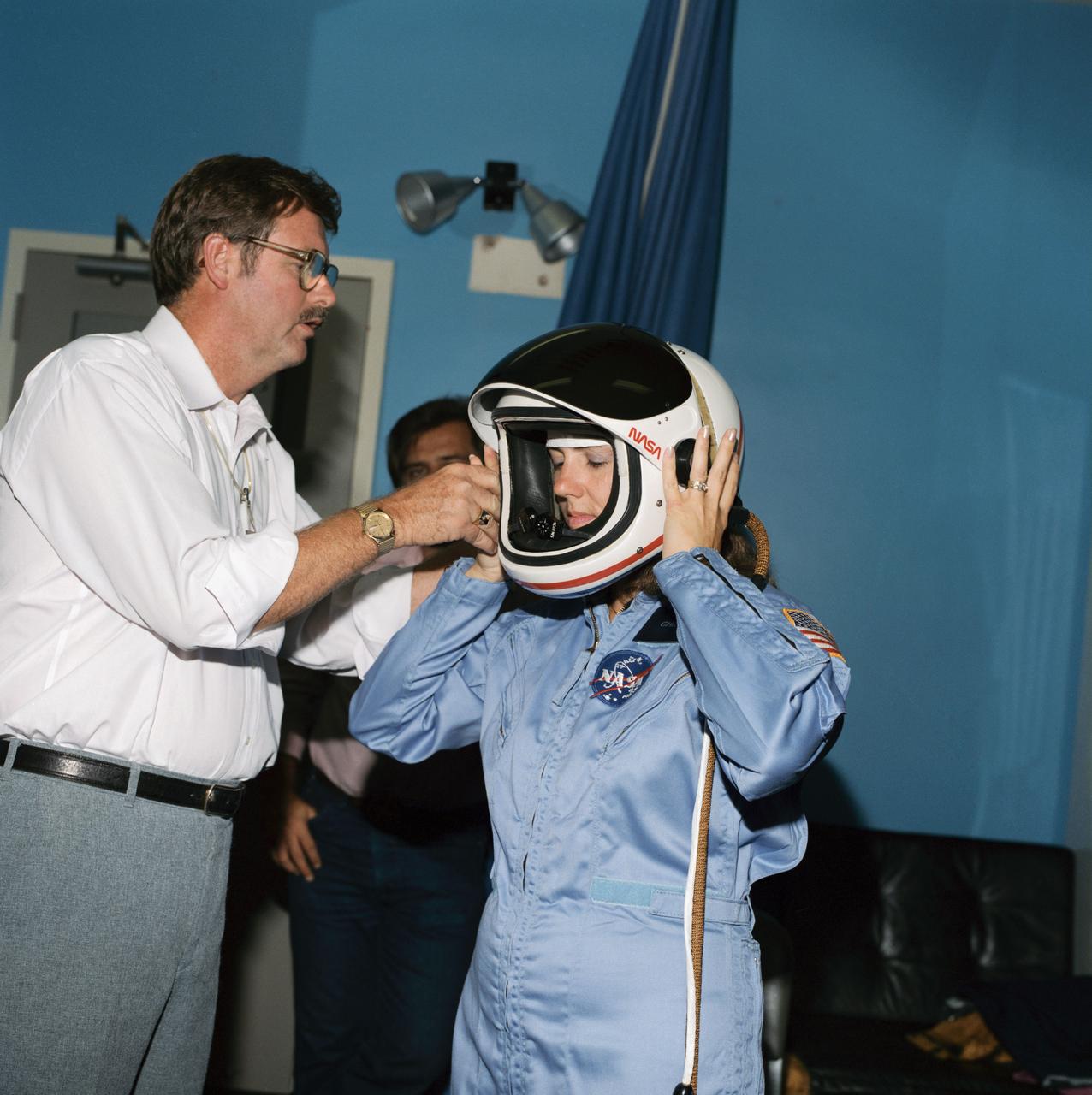 S85-40030 (November 1985) --- Payload specialist Sharon Christa McAuliffe is briefed on launch/entry helmets by crew systems technician Alan M. Rochford in the Johnson Space Center’s crew systems lab. McAuliffe is one of seven crew members in training for STS-51L flight scheduled for January 1986. Photo credit: NASA
