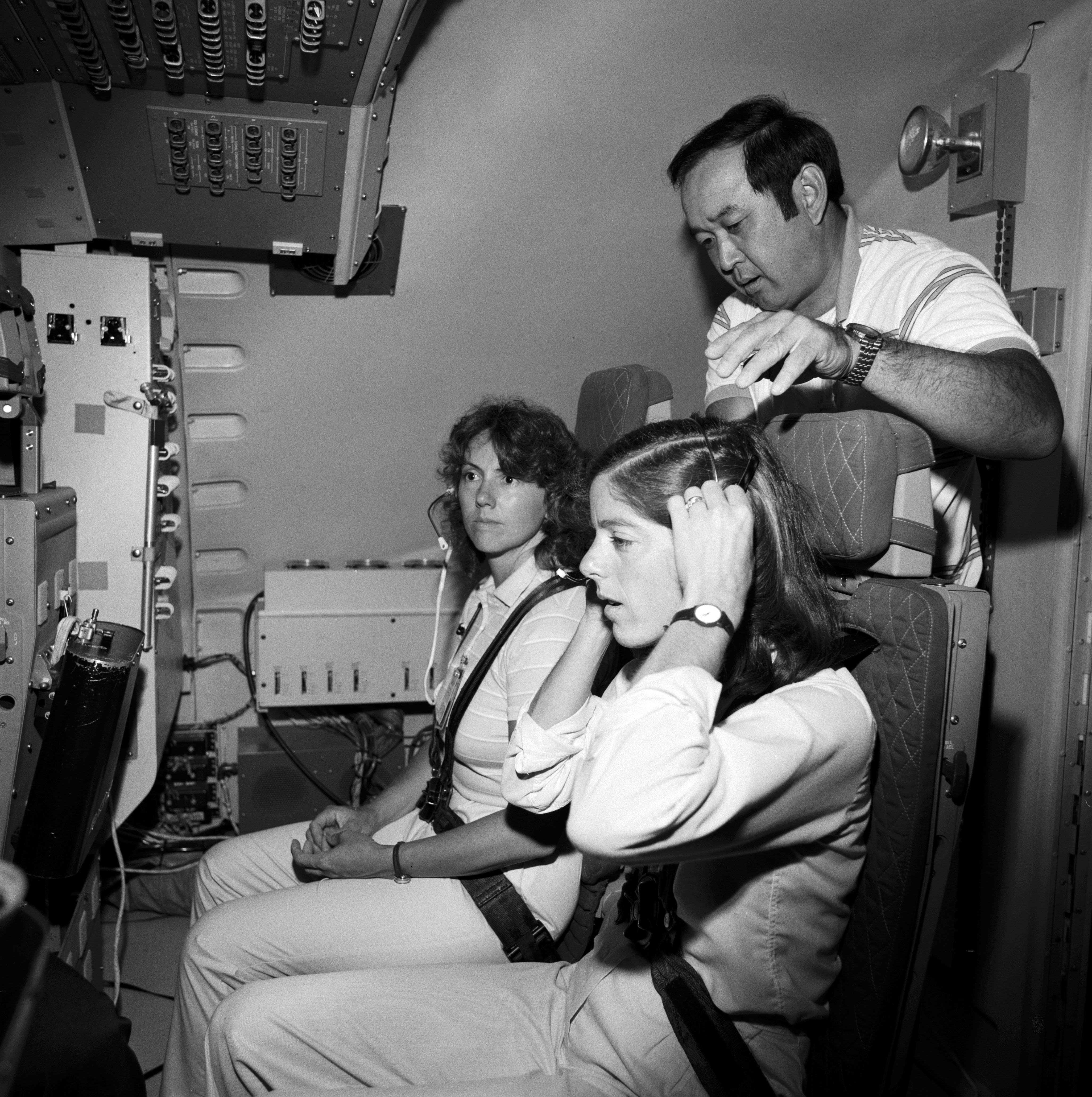 S85-40510 & S85-40511 (23 Sept. 1985) --- Two women representing the Teacher-in-Space Project undergo training in preparation for the 51-L mission in two photographs made in the Johnson Space Center’s mission simulation and training facility. In S85-40510, Sharon Christa McAuliffe (second right), prime crew member; and Barbara R. Morgan (second left), backup, are briefed in the shuttle mission simulator’s instruction station by Jerry Swain, right, instruction team leader. Others pictured are Michelle Brekke (far left) of the payload specialists’ office and Patricia A. Lawson (lower left foreground). Astronaut Ellison S. Onizuka, in S85-40511, assists Morgan with a head set as the two trainees are familiarized with launch and entry stations in the motion base shuttle mission simulator (SMS). The citizen observer (McAuliffe) is scheduled to be seated on the middeck. This picture, however, was taken at the mission specialists’ station on the flight deck. Photo credit: NASA