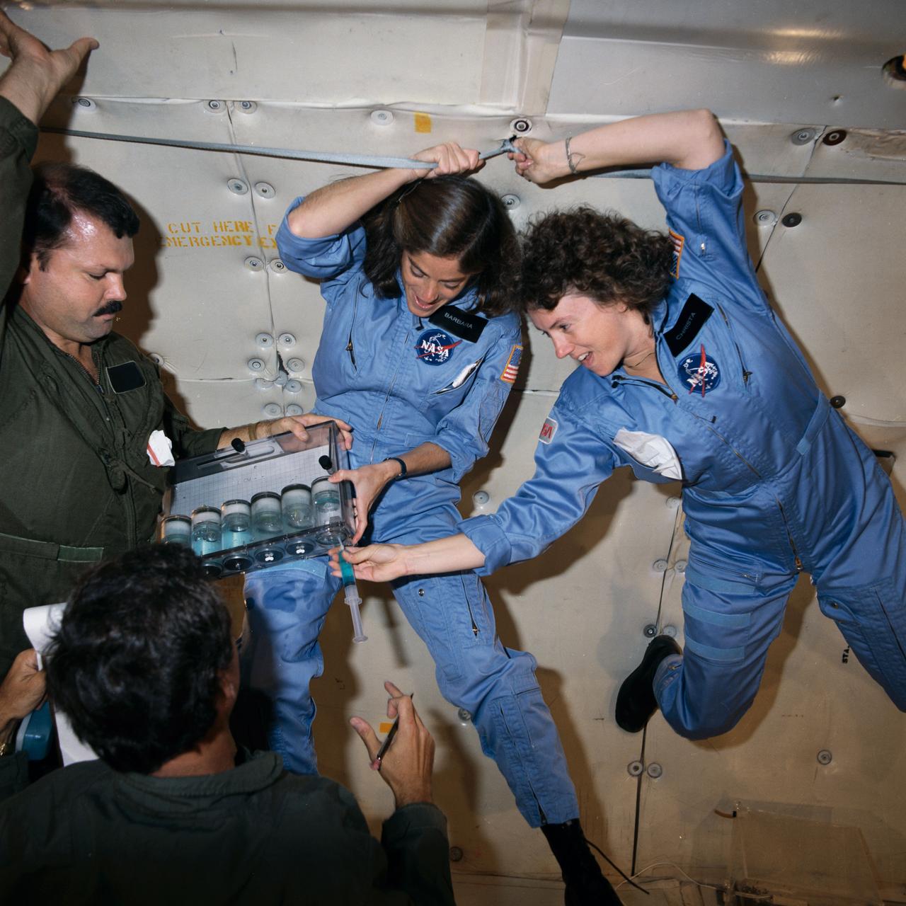 S85-42470 (16 Oct. 1985) --- Sharon Christa McAuliffe, right, and Barbara R. Morgan, participating in the Teacher-in-Space Project, team up with Bob Mayfield, a JSC aerospace educations specialist, to preview some experiments in zero-G. A KC-135 aircraft flies a special pattern to provide series of brief periods of weightlessness. McAuliffe, prime crew member for STS-51L, injects a hydroponic solution into a cylinder to review one of the experiments planned for the flight. Morgan is backup for McAuliffe on that mission. Photo credit: NASA