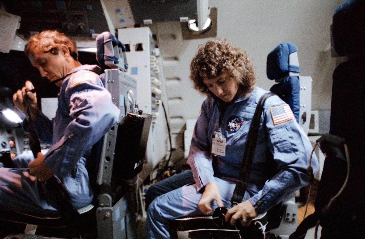 S85-44459 (19 Nov. 1985) --- Sharon Christa McAuliffe, seated behind 51-L pilot Michael J. Smith, prepares to strap herself into the mission specialists position in the Shuttle Mission Simulator (SMS) as part of her training for the 51-L mission. Photo credit: NASA