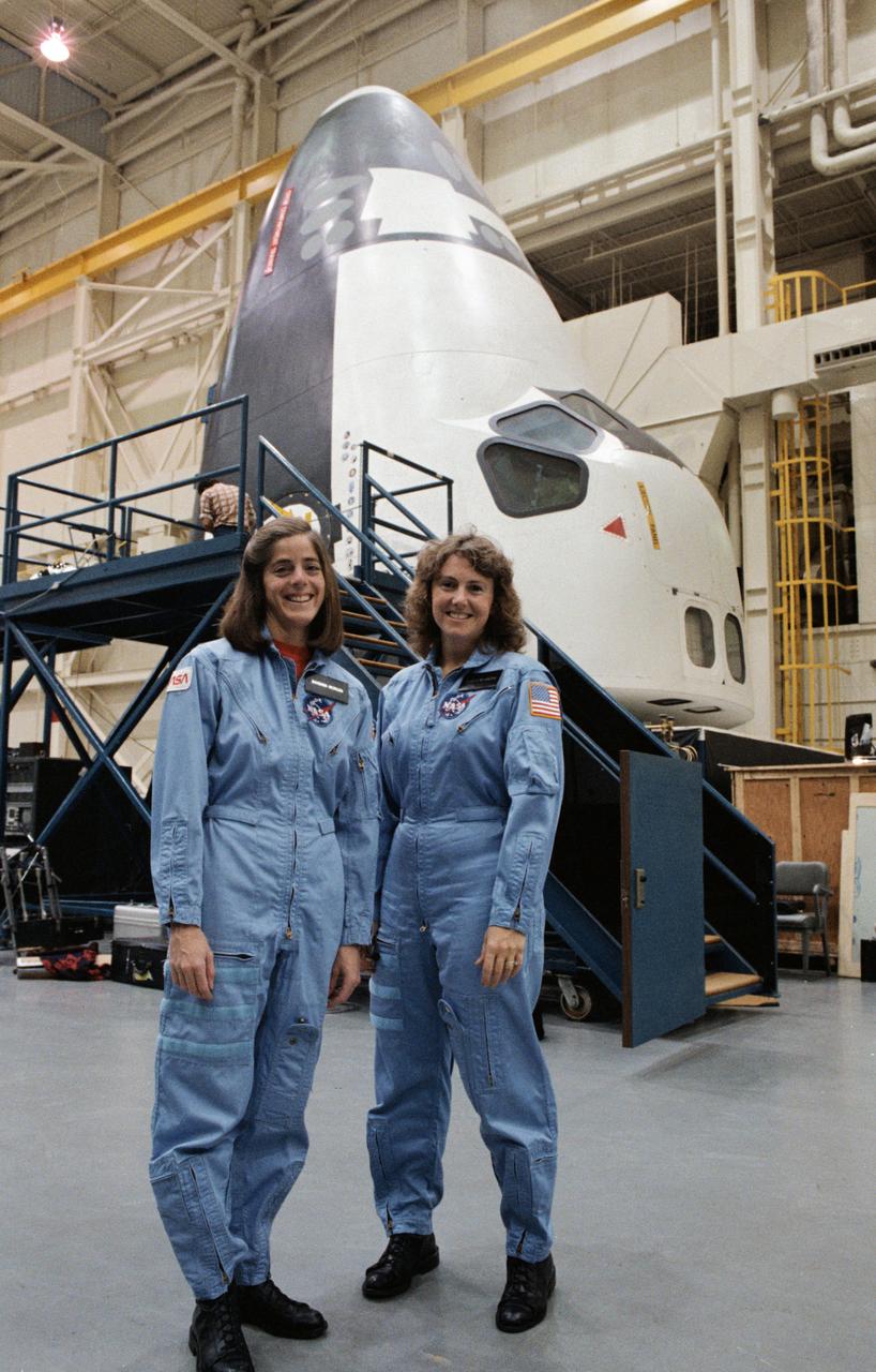 S85-46693 (26 Dec. 1985) --- Sharon Christa McAuliffe (right), the Teacher-in-Space payload specialist assigned to the STS-51L mission, and her backup, Barbara R. Morgan pose for photos after training in the shuttle mock-up and integration laboratory at JSC. The shuttle crew compartment, in a launch mode, can be seen in the background. Photo credit: NASA