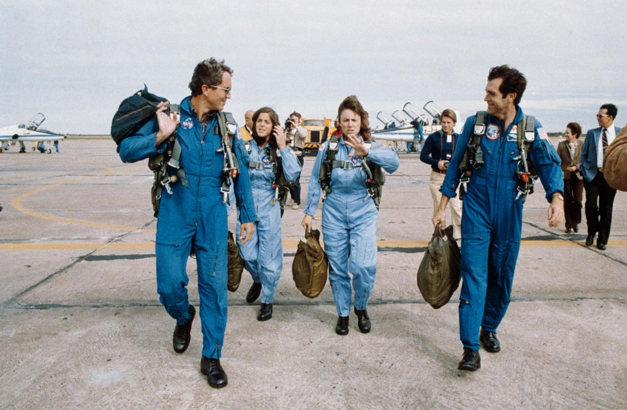 S86-25199 (September 1985) --- Three members of the STS-51L prime crew and a backup crew member walk away from the flight line at nearby Ellington Field following flights in the T-38 jet trainers seen in the background.  Sharon Christa McAuliffe (center right), payload specialist/citizen observer for the Teacher-in-Space Project, and Barbara R. Morgan (center left), her backup, are flanked by astronauts Francis R. (Dick) Scobee (right), mission commander, and Michael J. Smith, pilot. The photo was taken by Keith Meyers of the New York Times.    EDITOR?S NOTE: The STS-51L crew members lost their lives in the space shuttle Challenger accident moments after launch on Jan. 28, 1986 from the Kennedy Space Center (KSC). Photo credit: NASA
