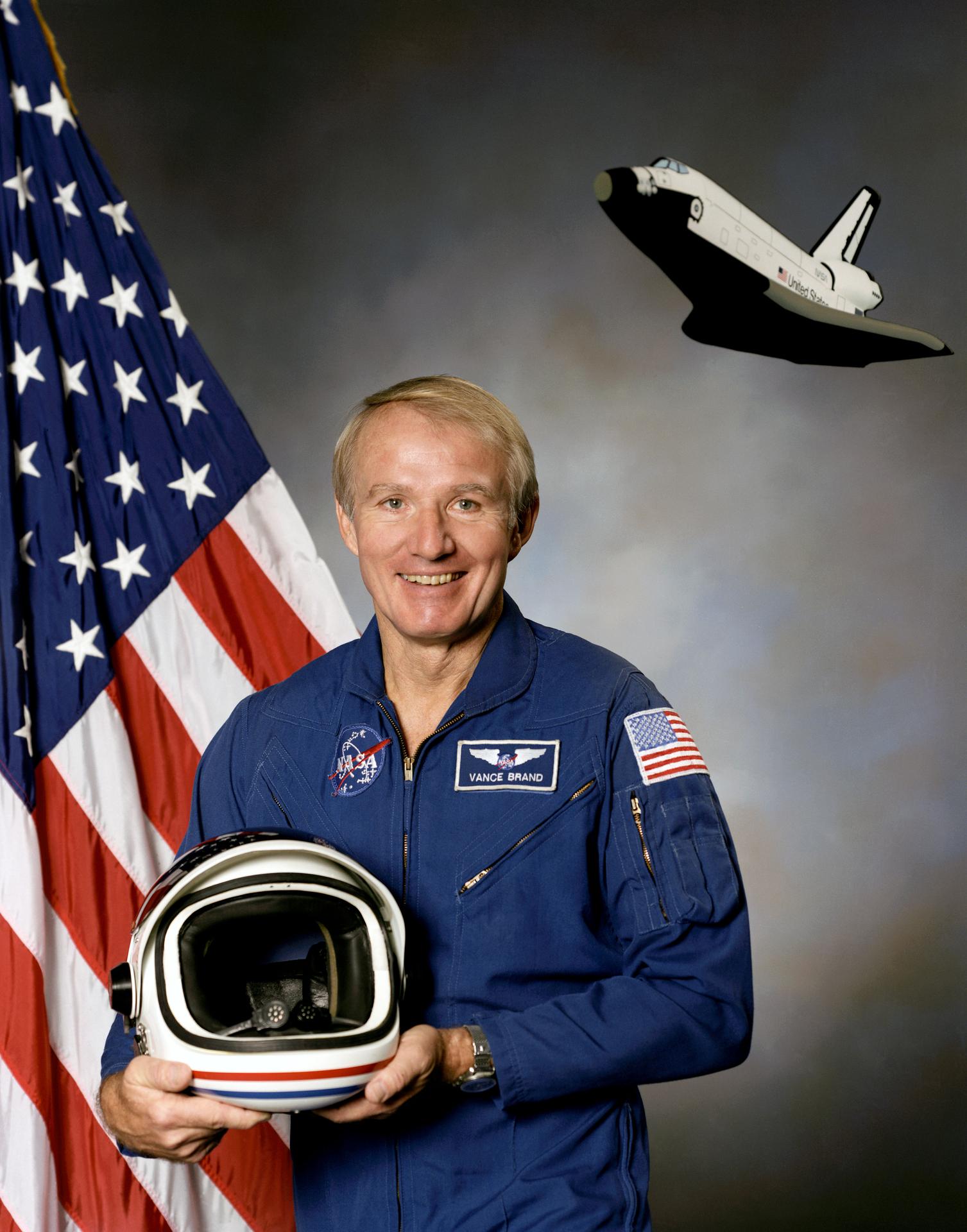 A man holds a spacesuit helmet and smiles before the American flag