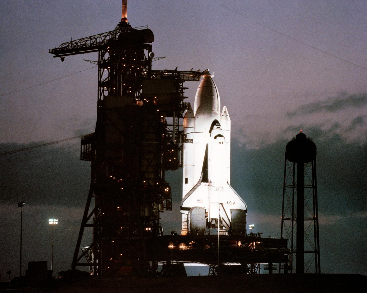 Space Shuttle Columbia, mated with its other Shuttle components, is attached     to the launching pad. Wide-angle view of the Columbia sitting on its launch      pad in the darkness. The launch complex is illuminated with lights along the     structure.      KSC, FL
