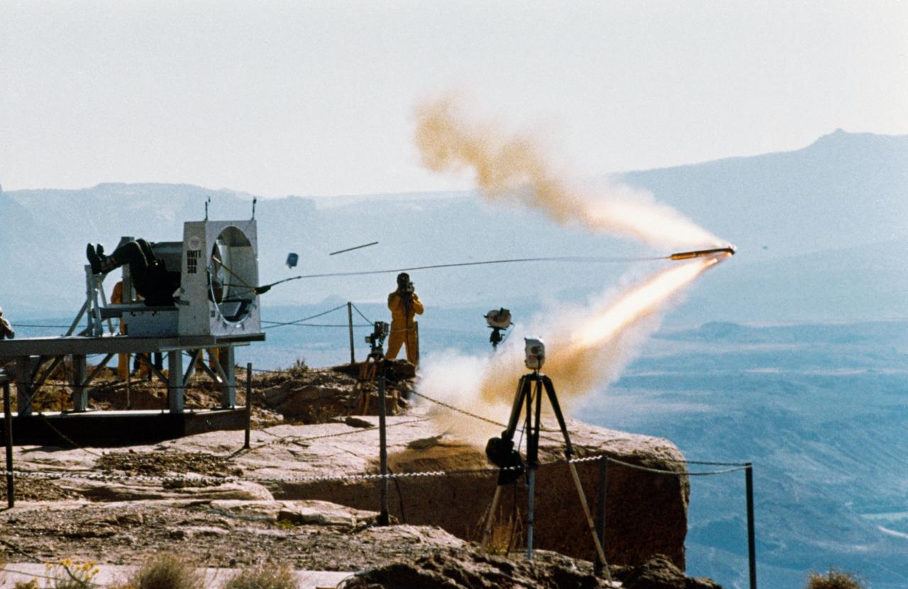 Shuttle crew escape systems (CES) tractor rocket tests conducted at Hurricane Mesa, Utah. This preliminary ground test of the tractor rocket will lead up to in-air evaluations. View shows tractor rocket as it is fired from side hatch mockup. The tractor rocket concept is one of two escape methods being studied to provide crew egress capability during Space Shuttle controlled gliding flight. In-air tests of the system, utilizing a Convair-240 aircraft, will begin 11-19-87 at the Naval Weapons Center in China Lake, California.