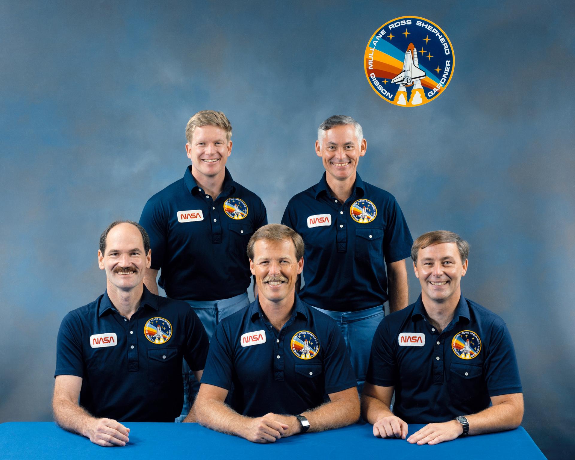 Five astronauts in blue shirts pose for crew portrait