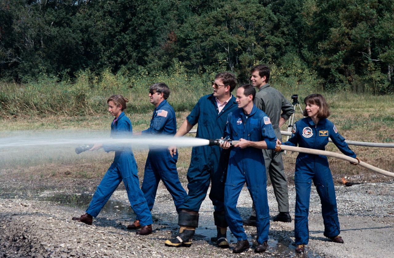 STS-32 crewmembers use water hoses during fire fighting exercises at JSC's Fire Training Pit across from the Gilruth Center Bldg 207. Mission Specialist (MS) G. David Low with nozzle open directs water into the fire as fire/ security personnel coaches and instructs him on his attempt to extinguish the blaze. MS Bonnie J. Dunbar maneuvers the hose behind Low. A second group of crewmembers alongside Low and Dunbar, MS Marsha S. Ivins, holding hose nozzle, Commander Daniel C. Brandenstein, and Pilot James D. Wetherbee position themselves before opening hose nozzle.