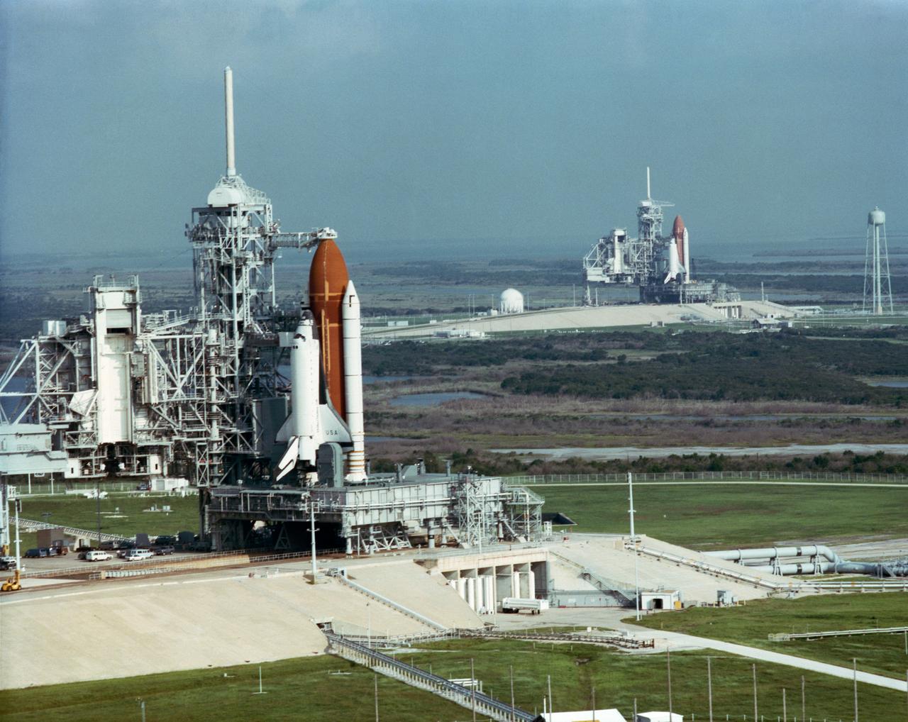 S90-48650 (5 Sept 1990) --- This rare view shows two space shuttles on adjacent pads at Launch Complex 39 with the Rotating Service Structures (RSR) retracted. Space Shuttle Columbia (foreground) is on Pad A where it awaits further processing for a September 6 early morning launch on STS-35. Discovery, its sister spacecraft, is set to begin preparations for an October liftoff on STS-41 when the Ulysses spacecraft is scheudled to be taxied into space. PLEASE NOTE:  Following the taking of this photograph, STS-35 was postponed and STS-41's Discovery was successfully launched on Oct. 6.