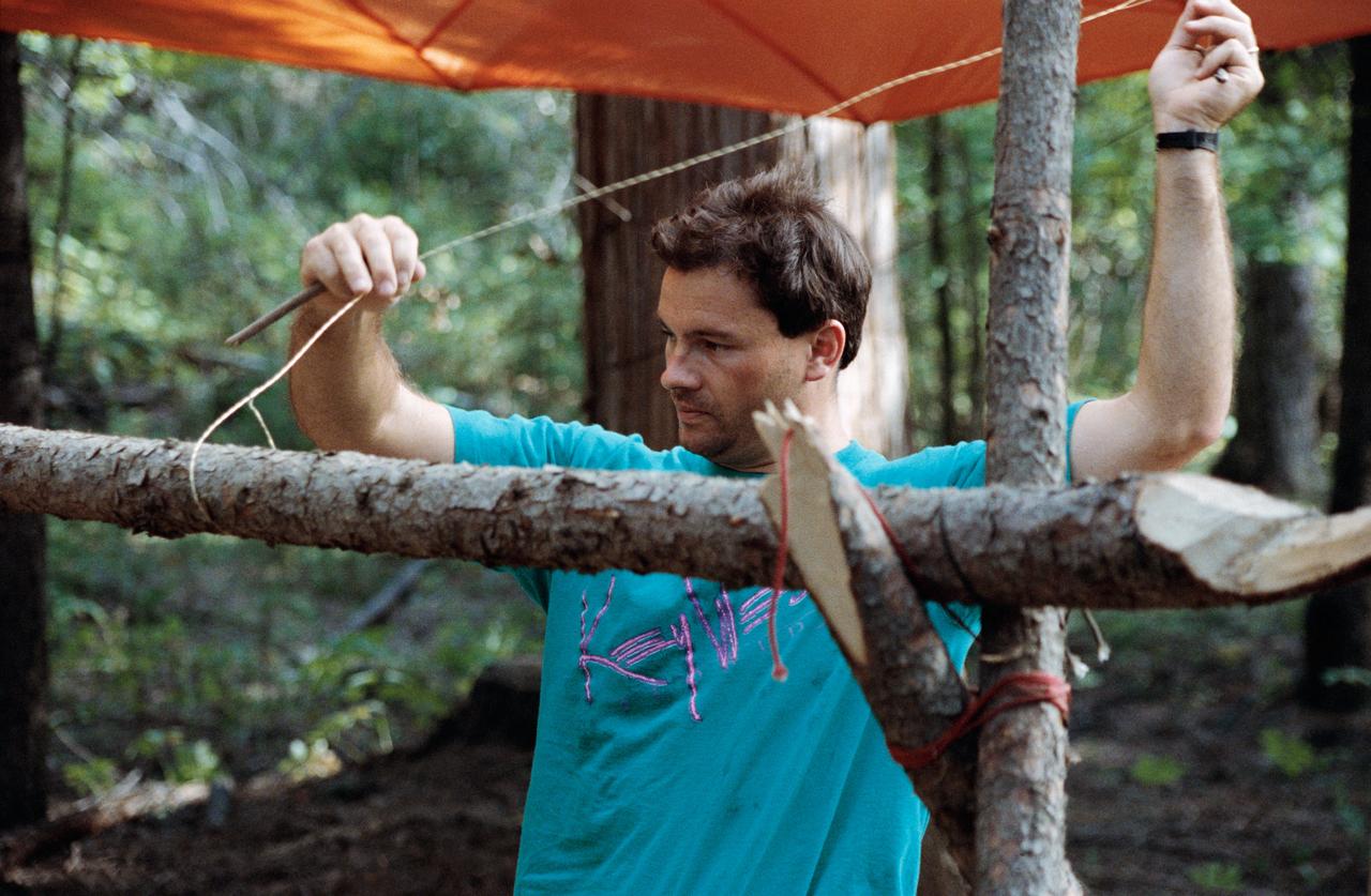 S92-46167 (16-20 Aug. 1992) --- Michael E. Lopez-Alegria, one of 19 astronaut candidates announced in March, fashions a shelter from wood and parachute material.  He was taking in a four-day wilderness survival training course at Fairchild Air Force Base in Washington.  Lopez-Alegria and his class mates had reported to the Johnson Space Center (JSC) in Houston, Texas, for initial training and evaluation earlier this month.        EDITOR?S NOTE: Lopez-Alegria has been named fly aboard the Space Shuttle Columbia for the STS-73 mission, scheduled for 1995
