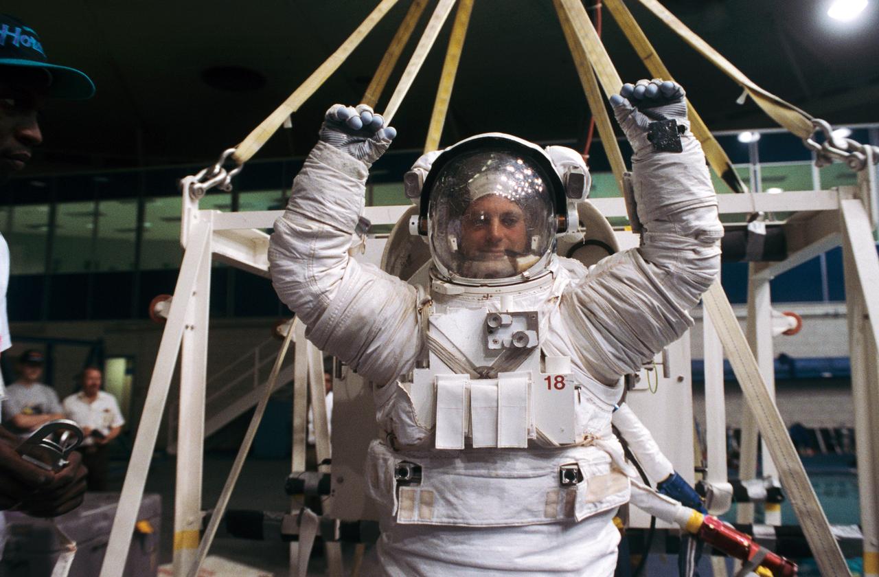 S93-31701 (3 April 1993) --- Displaying the flexibility of his training version of the Shuttle Extravehicular Mobility Unit (EMU) space suit, astronaut David A. Wolf participates in training for contingency Extravehicular Activity (EVA) for the STS-58 mission.  Behind Wolf, sharing the platform with him was astronaut Shannon W. Lucid.  For simulation purposes, the two mission specialists were about to be submerged to a point of neutral buoyancy in the Johnson Space Center's (JSC) Weightless Environment Training Facility (WET-F).  Though the Spacelab Life Sciences (SLS-2) mission does not include a planned EVA, all crews designate members to learn proper procedures to perform outside the spacecraft in the event of failure of remote means to accomplish those tasks.