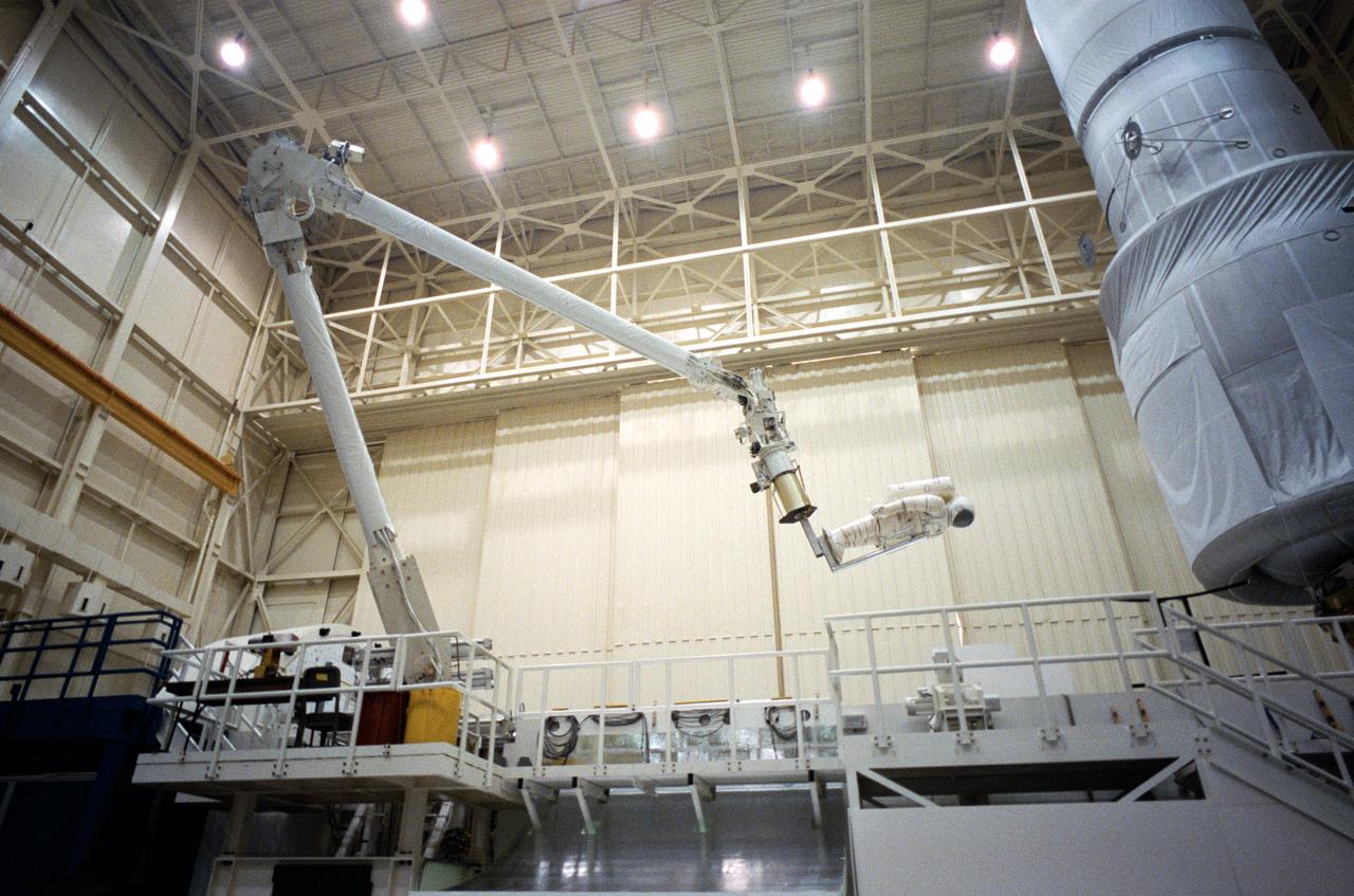 The Remote Manipulator System (RMS) eases a mannequin representing an astronaut into position for an STS-61 Hubble Space Telescope (HST) servicing task in the Space Shuttle mockup and integration laboratory at JSC (35699, 35703); Wide-angle view of the RMS easing a mannequin into position for work on the HST mock-up in bldg 9N (35700-1); Swiss scientist Claude Nicollier, mission specialist, works the control of the RMS during a training session in the manipulator development facility (MDF) in JSC's Shuttle mock-up and integration laboratory. Astronaut Kenneth D. Bowersox (left), pilot, is among the other crewmembers in training for the STS-61 HST servicing mission (35702).