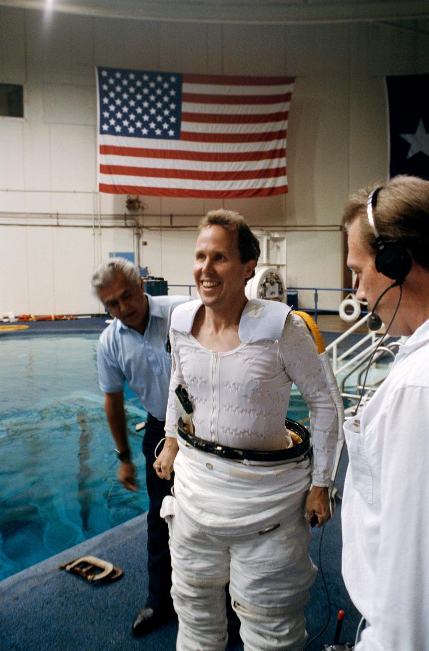 Astronaut Thomas D. Jones, mission specialist, dons a space suit prior to participating in contingency space walk simulations at the JSC Weightless Environment Training Facility (WETF). Jones is assisted by Frank Hernandez (left) and suit technician Charles Hudson of Hamilton Standard. Jones suit is weighted to that he can achieve a neutrally buoyant state once under water. Extravehicular tasks are not planned for the STS-59 mission, but a number of chores are rehearsed in case of failure of remote systems to perform those jobs.