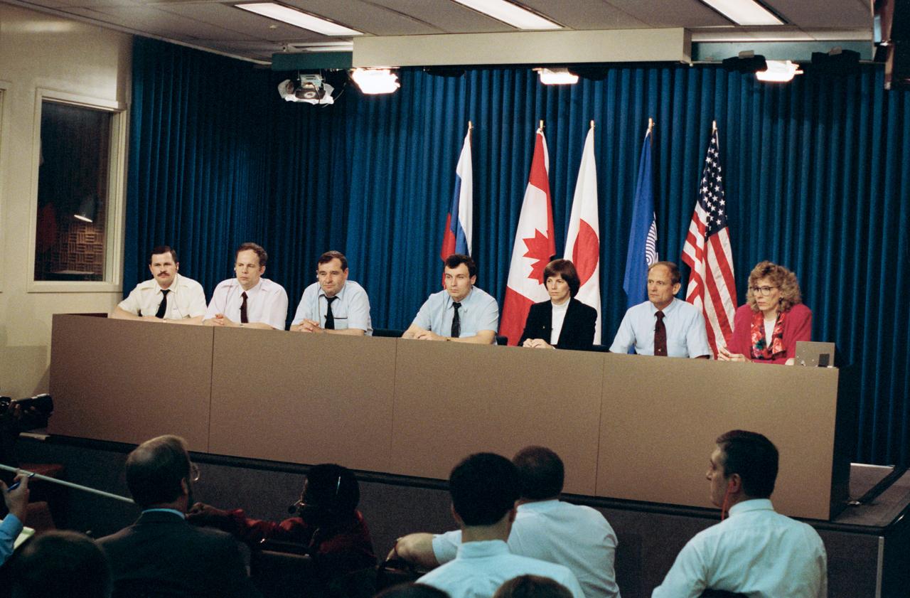 Crew members for the joint Space Shuttle / Mir mission field questions from the press at JSC. Left to right are cosmonauts Nikolai M. Budarin, Anatoliy Y. Solovyov, Gennadiy M. Strekalov, Vladimir N. Dezhurov, and astronauts Bonnie J. Dunbar, Norman E. Thagard, along with Kari L. Fluegel of the Public Affairs Office's (PAO) News and Media Services Branch. Flags representing the international space partners - Russia, the United States, the European Space Agency (ESA), Canada and Japan - are displayed behind the conference participants.