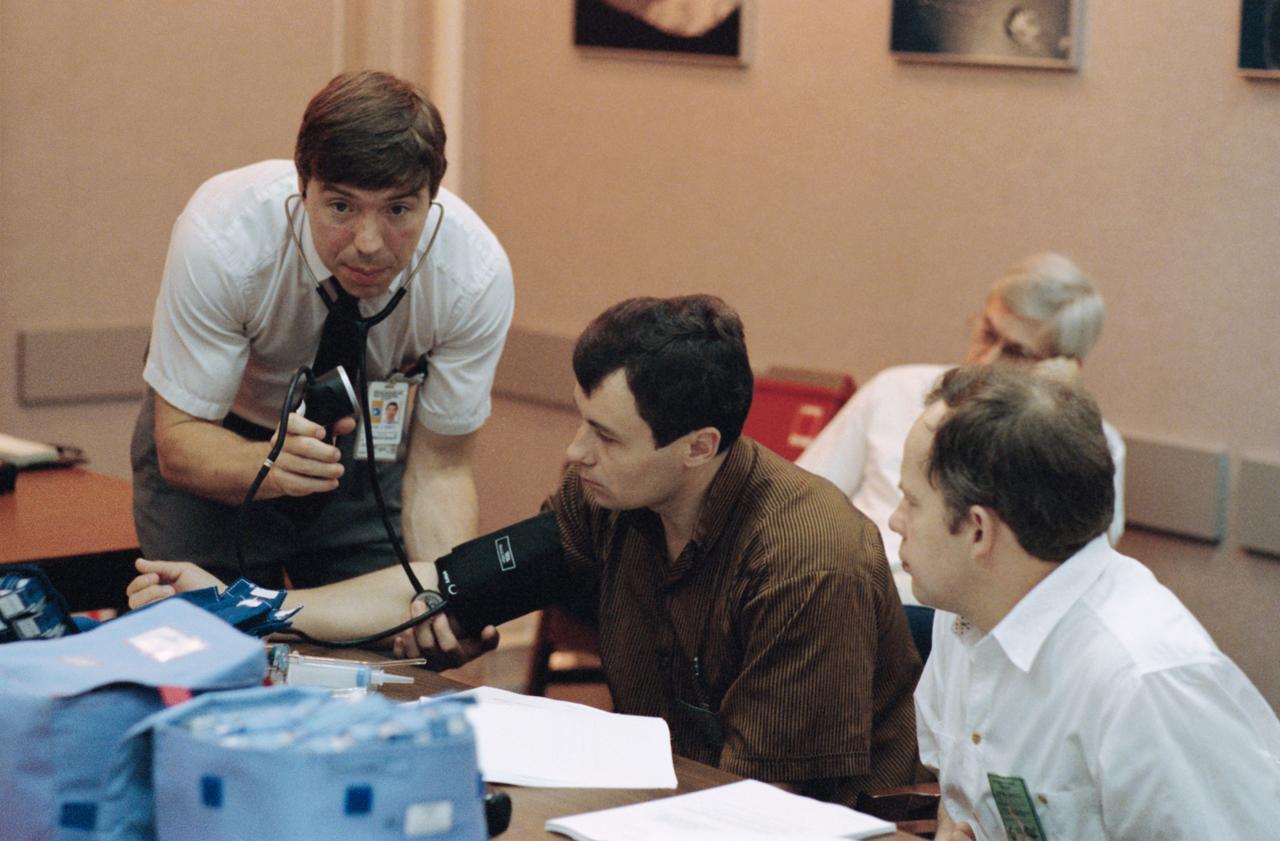 Cosmonaut Vladimir N. Dezhurov (center), Mir 18 mission commander, gets his blood pressure taken by Dr. Michael J. Barrett, flight surgeon. Cosmonaut Anatoliy Y. Solovyev (right), Mir 19 mission commander, looks on. Solovyev, Dezhurov, along with their respective flight engineers and a number of other cosmonauts and astronauts participating in the joint program, were in Houston, Texas, to prepare for their upcoming missions.