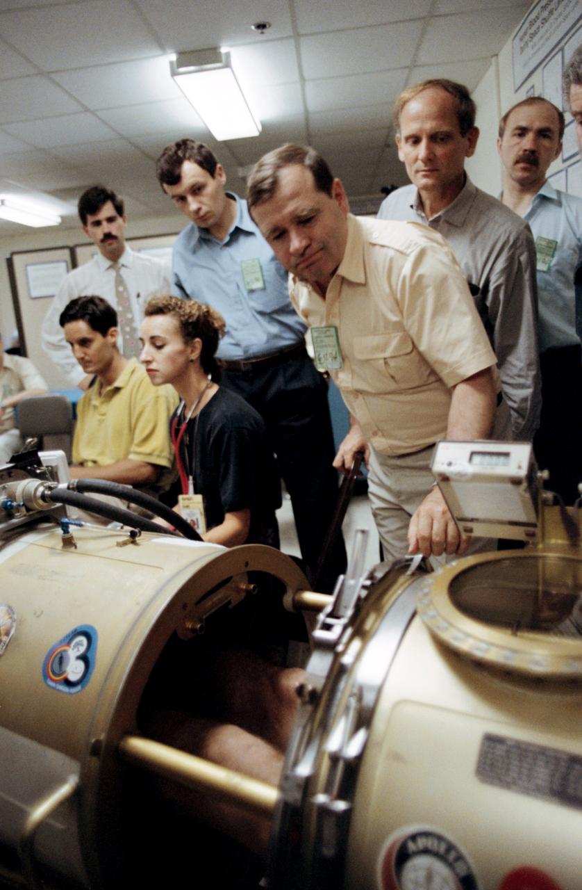 Astronaut Norman E. Thagard (right center), a guest researcher on Russia's Mir 18 mission, monitors a test of a subject (out of frame) in the Lower Body Negative Pressure (LBNP) device. Others pictured, left to right, are Todd Schlegel (seated) of the Medical Sciences Division at JSC, unidentified trainer, Linda Barrows of Krug; cosmonaut Vladimir N. Dezhurov, mission commander; cosmonaut Gennadiy M. Strekalov, Thagard and cosmonaut Alexsandr F. Poleshchuk, Mir 18 reserve flight engineer.