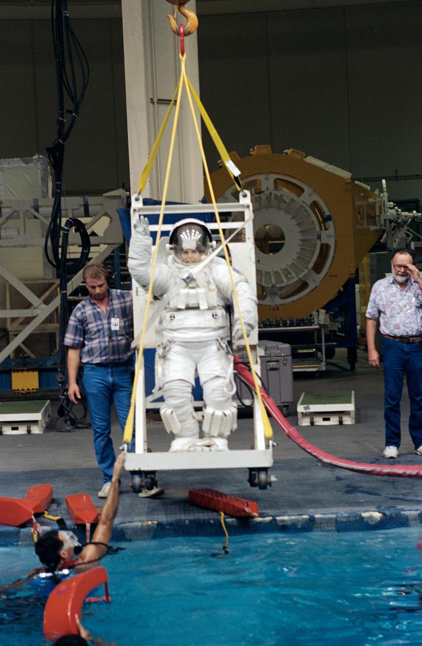 Attired in a training version of the Extravehicular Mobility Unit (EMU), Astronaut Mary Ellen Weber participates in a training session at JSC's Weightless Environment Training Facility (WETF). Training as a mission specialist for the STS-70 mission, Weber was about to rehearse a contingency space walk. One of several SCUBA-equipped divers waits to assist in the rehearsal in the water.