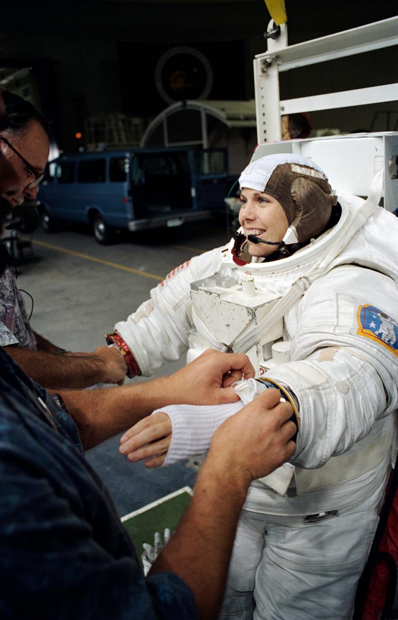 Attired in a training version of the Extravehicular Mobility Unit (EMU), astronaut Mary Ellen Weber gets help with the final touches of suit donning during a training session at JSC's Weightless Environment Training Facility (WETF). Training as a mission specialist for the STS-70 mission, Weber was about to rehearse a contingency space walk.