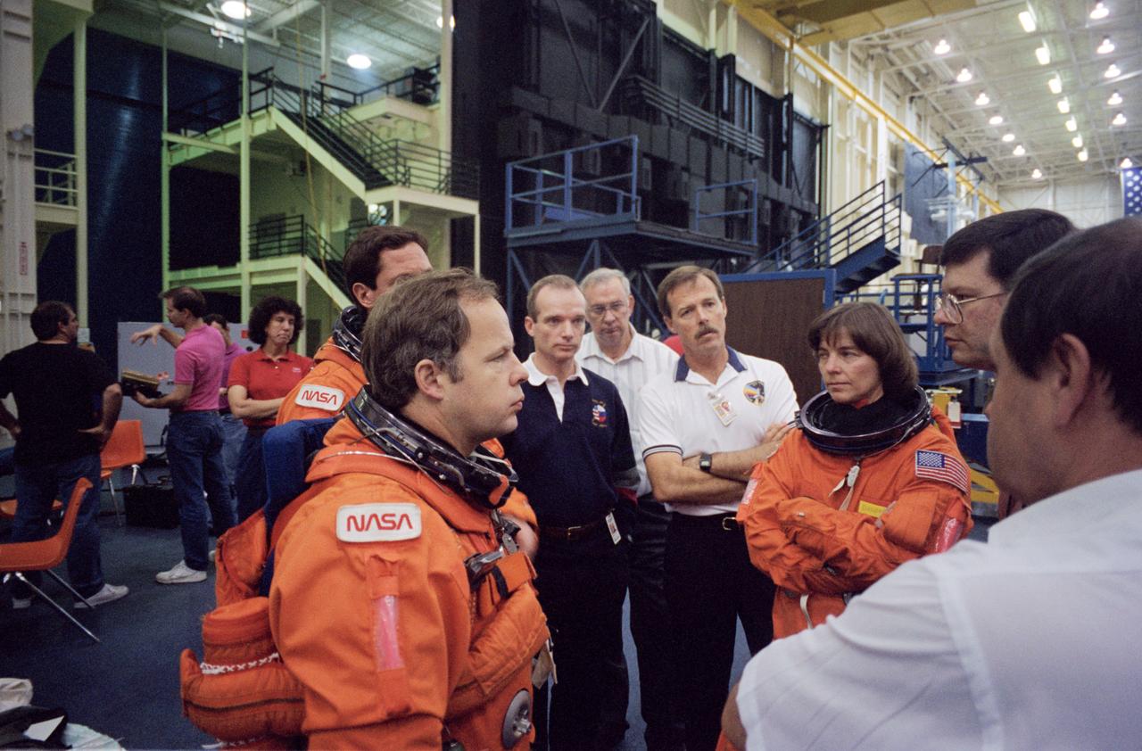 S94-47079 (18 Oct 1994) --- Astronaut Robert L. Gibson, (arms folded, near center) STS-71 mission commander, joins several crew mates during a briefing preceding emergency egress training in the Systems Integration Facility at the Johnson Space Center (JSC).  Astronauts Bonnie J. Dunbar and Gregory J. Harbaugh (partially obscured), along with cosmonaut Anatoliy Y. Solovyev, all mission specialists, are attired in training versions of the partial pressure launch and entry space suits.  Astronaut Charles J. Precourt, pilot, is in center foreground, and Ellen S. Baker, mission specialist, is in left background.
