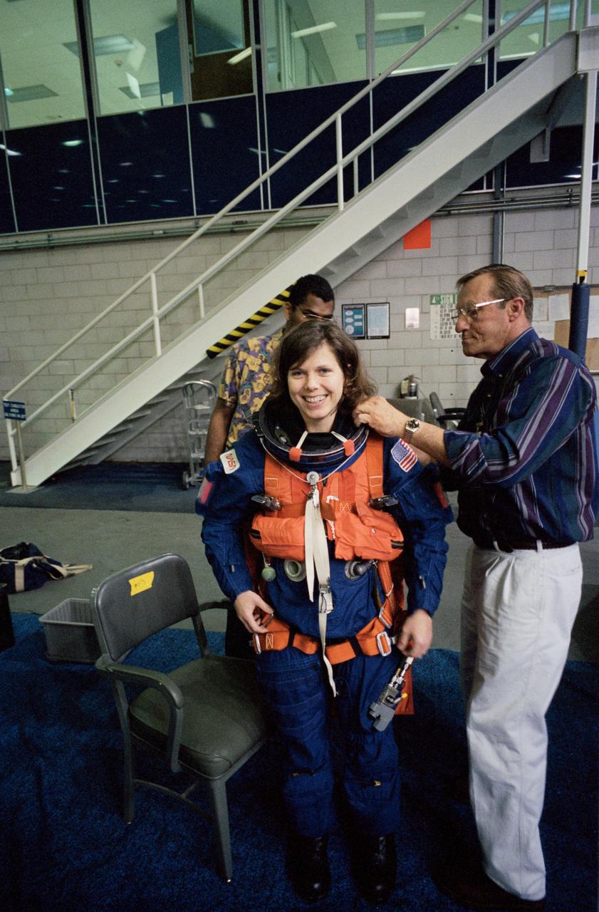 S95-03469 (16 FEB 1995) --- Attired in a training version of the Shuttle launch and entry garment, astronaut Mary Ellen Weber gets help with the final touches of suit donning during a training session at the Johnson Space Center's (JSC) Weightless Environment Training Facility (WET-F).  Helping out is Rockwell's William L. Todd (right), while Staffon Isaacs looks on.  Training as a mission specialist for the STS-70 mission, Weber was about to rehearse emergency bailout.  The crew members made use of a nearby 25-feet deep pool to practice parachute landings in water and subsequent deployment of life rafts.