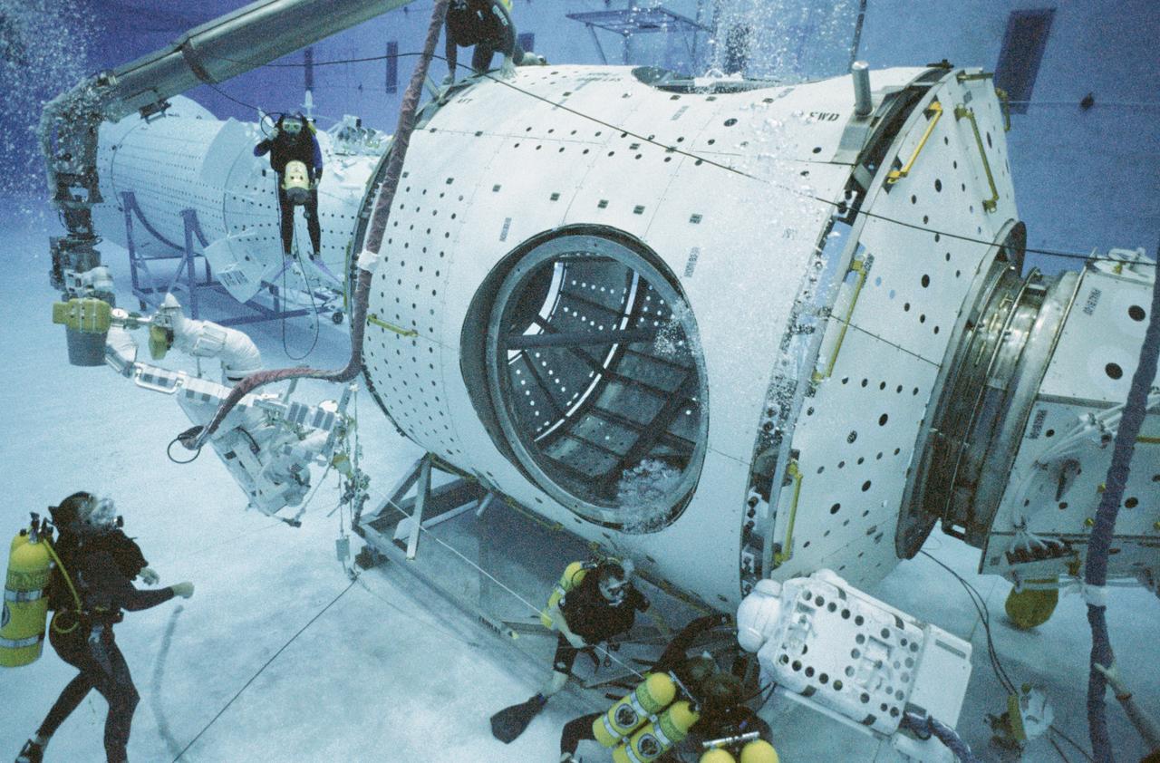 S97-11949 (8 Sept 1997) --- Wearing training versions of the Shuttle Extravehicular Mobility Unit (EMU) space suit, astronauts Jerry L. Ross (left), and James Newman perform the first training session in the Neutral Buoyancy Laboratory (NBL) of the Sonny Carter Training Facility. The training was actually a dress rehearsal of three Extravehicular Activity?s (EVA) the pair will conduct during the July 1998 flight (STS-88) -- the first International Space Station (ISS) assembly mission. During the six-hour training session, the crew practiced hooking up power and data cables between full-scale mockups of the Functional Cargo Block and the United States-built Node 1 (foreground).