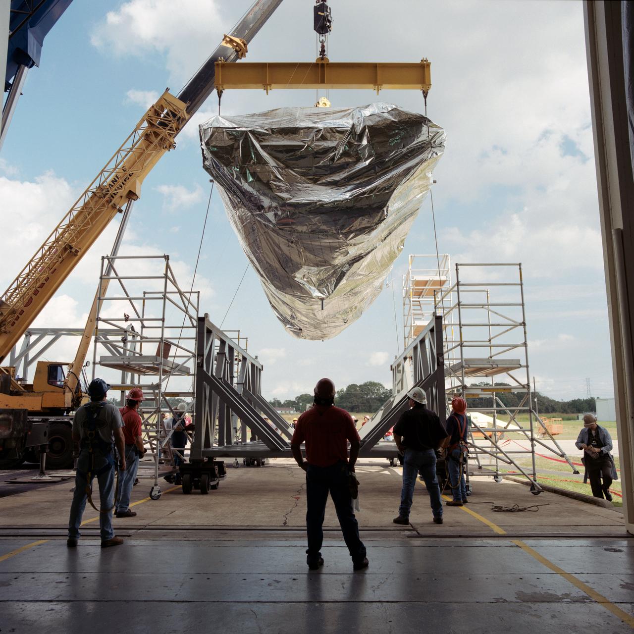The S0 Truss is moved into the highbay of bldg 49 for Space Station Module acoustic test. Views include: S0 Truss moved into bldg 49 highbay (17342-53, 17370-71); a measuring stick is held near Truss (17354); Truss in acoustic chamber (17355-61, 17367); Truss in air above cradle (17362, 17364-66, 17368); Truss in cradle (17363).