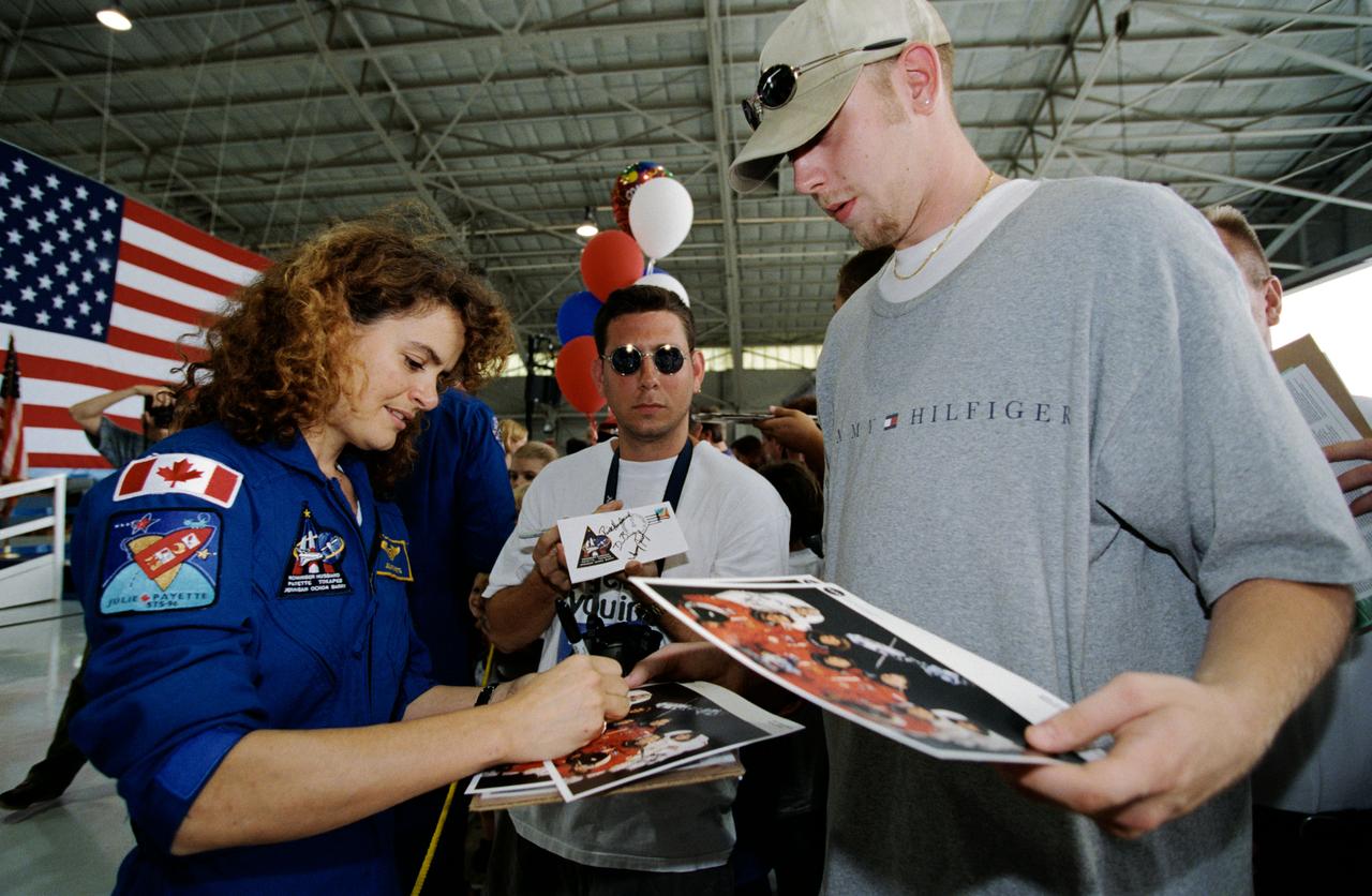 Photographic documentation showing the STS-96 crew return ceremony at Ellington Field. Views include: pilot Rick D. Husband with his two children, Mission Specialist (MS) Daniel T. Barry is partially visible behind him (05966); MS Ellen Ochoa holds a baby (05967); slanted side view of the stage with mission commander Kent V. Rominger at the podium, and seated behind him (left to right): Mr. George Abbey, JSC director, MS Valery Tokarev, MS Julie Payette, MS Daniel T. Barry, MS Ellen Ochoa, MS Tamara E. Jernigan and pilot Rick D. Husband (05968); Payette sign photographs for visitors (05969); Tokarev at the podium (05970); Husband at the podium (05971); Ochoa at the podium (05972); Rominger at the podium (05973); Tokarev signs photographs for visitors (05974); front, wide shot showing MS Tamara E. Jernigan at the podium, and seated behind her (left to right); Mr. George Abbey, MS Valery Tokarev, MS Julie Payette, MS Daniel T. Barry, MS Ellen Ochoa, pilot Rick D. Husband and mission commander Kent V. Rominger (05975); Jernigan signs photographs for visitors (05976).