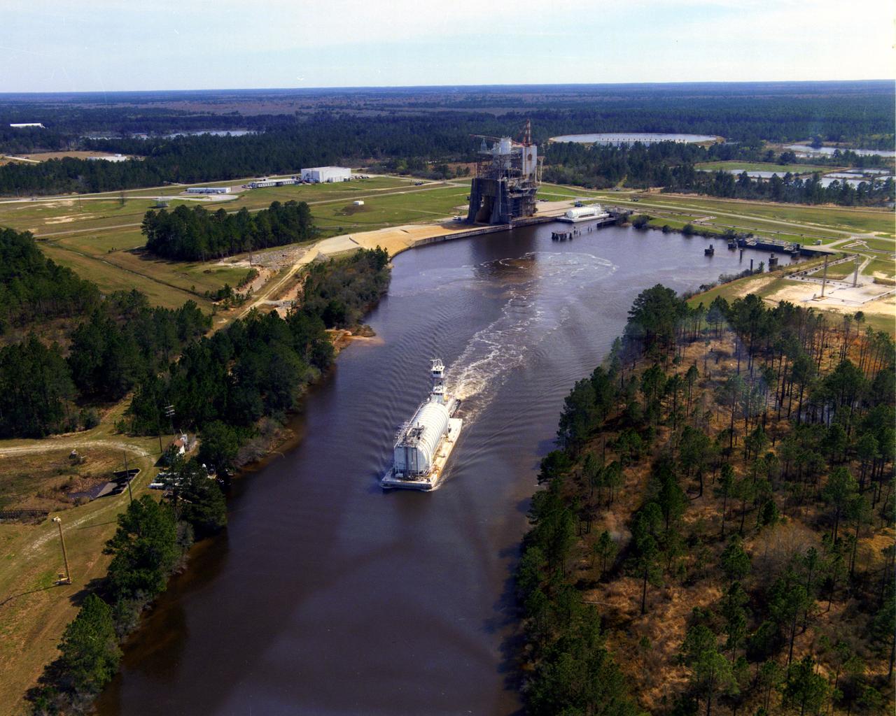 In this aerial view, a barge can be seen towing a container away from a test stand at the John C. Stennis Space Center.