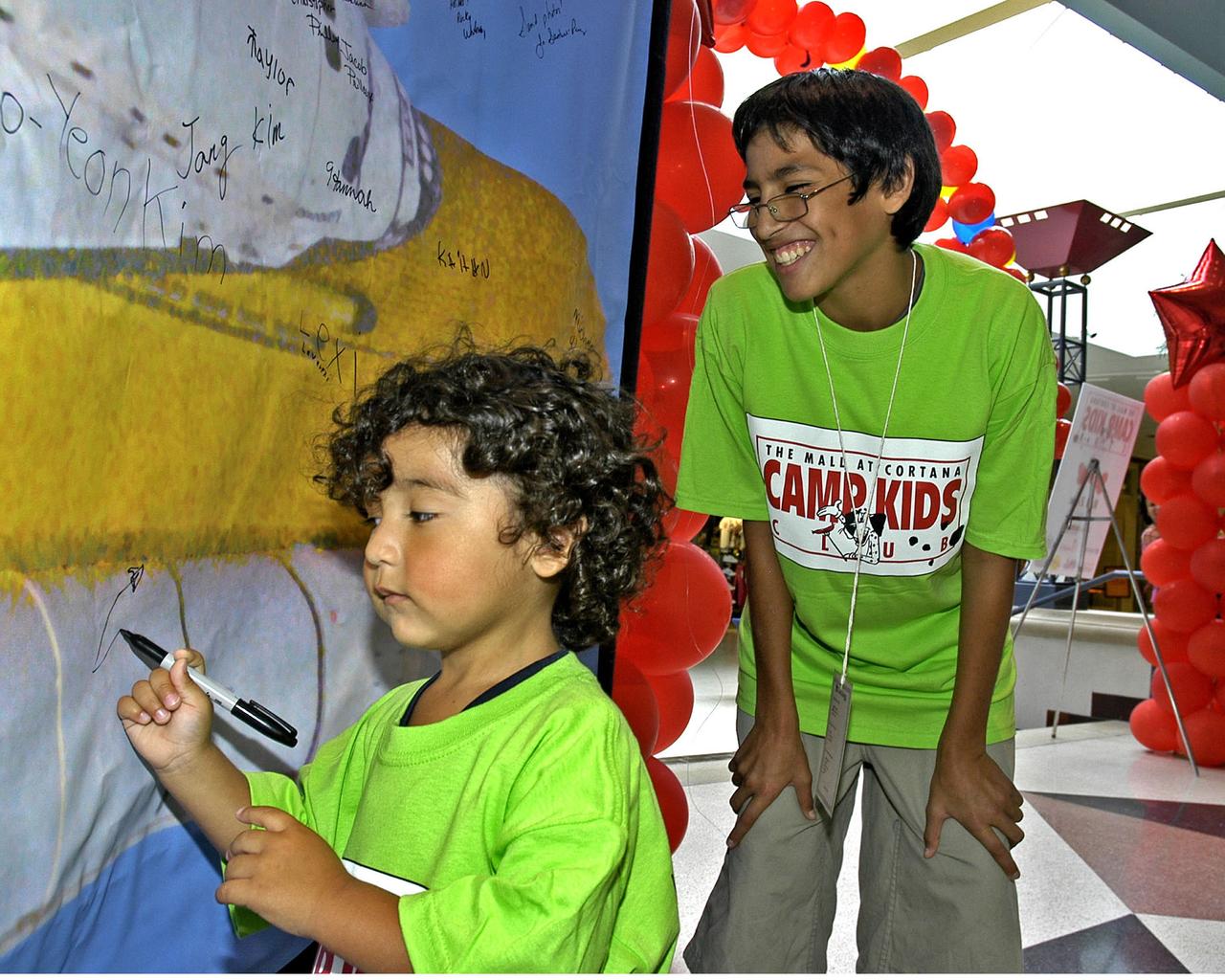 Christian Gonzales, 11 (right), watches as his little brother Walter, 2, adds his own brand of good wishes to a banner encouraging the crew of Space Shuttle Discovery on NASA's Return to Flight mission, scheduled to launch in summer 2005. The brothers, of Baton Rouge, were participating in a Camp Kids event at The Mall at Cortana, where Return to Flight activities were presented by NASA's Stennis Space Center (SSC).