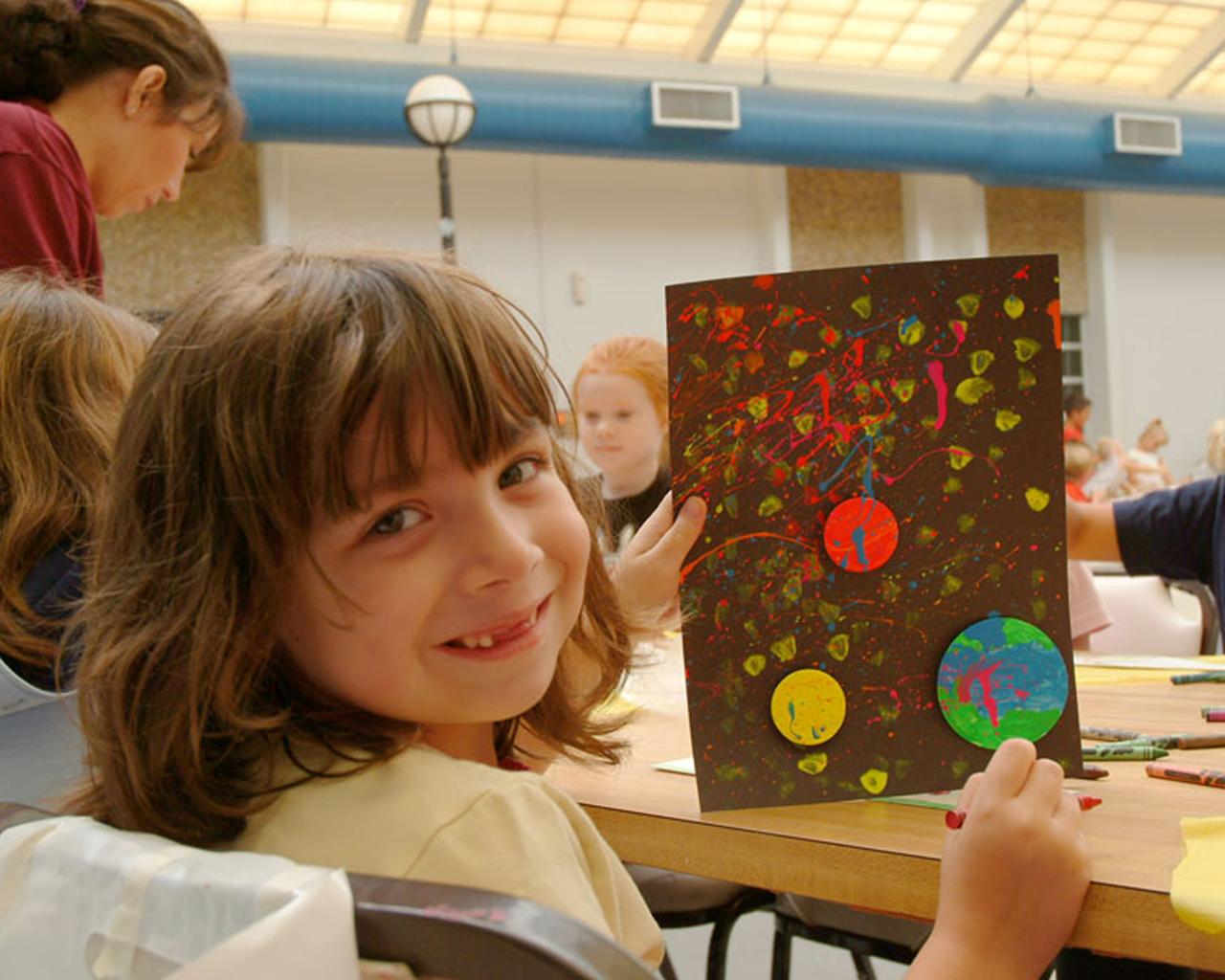 Sara Beth Casey, 5, proudly displays her artwork, 'Planets.' Sara Beth created the art as a student of Stennis Day Camp, a free camp for Stennis Space Center employees' children whose schools have not resumed since Hurricane Katrina hit the region on Aug. 29. The camp has registered nearly 200 children and averages 100 children each day. The camp will continue until all schools are back in session.