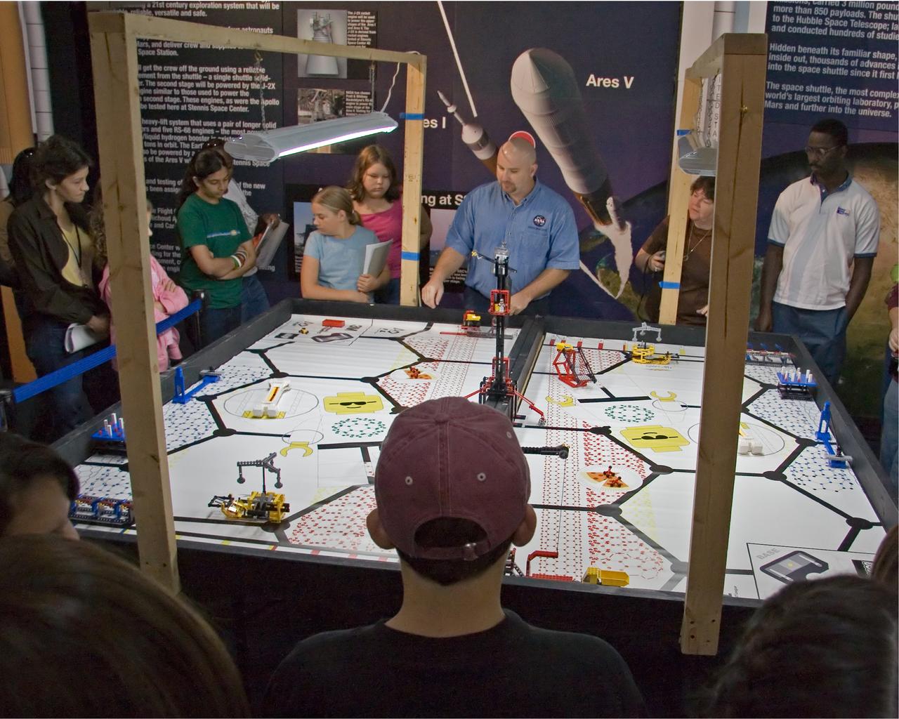 FIRST LEGO League participants listen to Aerospace Education Specialist Chris Copelan explain the playing field for 'Nano Quest' during a recent FLL kickoff event at StenniSphere, the visitor center at NASA Stennis Space Center. The kickoff began the 2006 FLL competition season. Eighty-five teachers, mentors, parents and 9- to 14-year-old students from southern and central Mississippi came to SSC to hear the rules for Nano Quest. The challenge requires teams to spend eight weeks building and programming robots from LEGO Mindstorms kits. They'll battle their creations in local and regional competitions. The Dec. 2 competition at Mississippi Gulf Coast Community College will involve about 200 students. FIRST LEGO League, considered the 'little league' of the FIRST (For Inspiration and Recognition of Science and Technology) Robotics Competition, partners FIRST and the LEGO Group. Competitions aim to inspire and celebrate science and technology using real-world context and hands-on experimentation, and to promote the principles of team play and gracious professionalism. Because NASA advocates robotics and science-technology education, the agency and SSC support FIRST by providing team coaches, mentors and training, as well as competition event judges, referees, audio-visual and other volunteer staff personnel. Two of Mississippi's NASA Explorer Schools, Bay-Waveland Middle and Hattiesburg's Lillie Burney Elementary, were in attendance. The following schools were also represented: Ocean Springs Middle, Pearl Upper Elementary, Long Beach Middle, Jackson Preparatory Academy, North Woolmarket Middle, D'Iberville Middle, West Wortham Middle, Picayune's Roseland Park Baptist Academy and Nicholson Elementary, as well as two home-school groups from McComb and Brandon. Gulfport and Picayune Memorial-Pearl River high schools' FIRST Robotics teams conducted robotics demonstrations for the FLL crowd.
