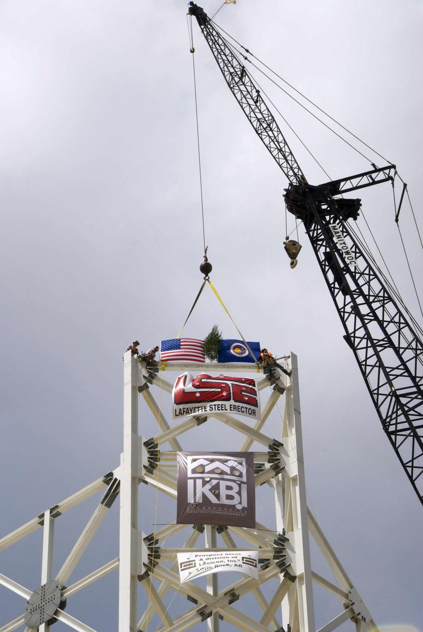 The final structural steel beam, bearing flags and the names of project workers, is hoisted and fastened into place atop the A-3 Test Stand.