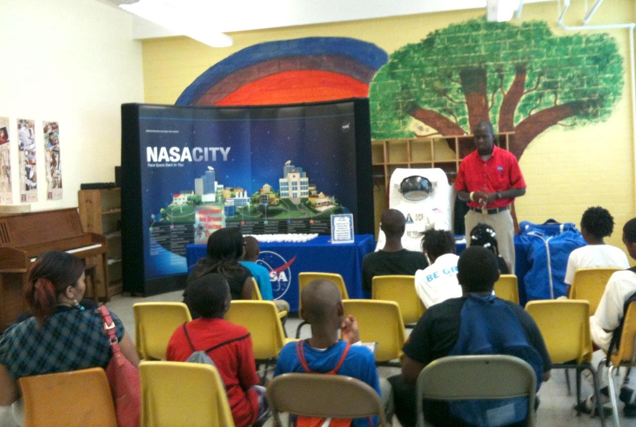 A Stennis Space Center employee talks to young people gathered for a NASA outreach activity at the Boys and Girls Club in Yazoo City, Miss., on June 5, 2012. The Stennis Office of External Affairs hosted outreach activities during a farmers' market in Canton on June 2 prior to visiting Yazoo City. In each instance, visitors were able to collect information about NASA, rocket engine testing and other work at Stennis.