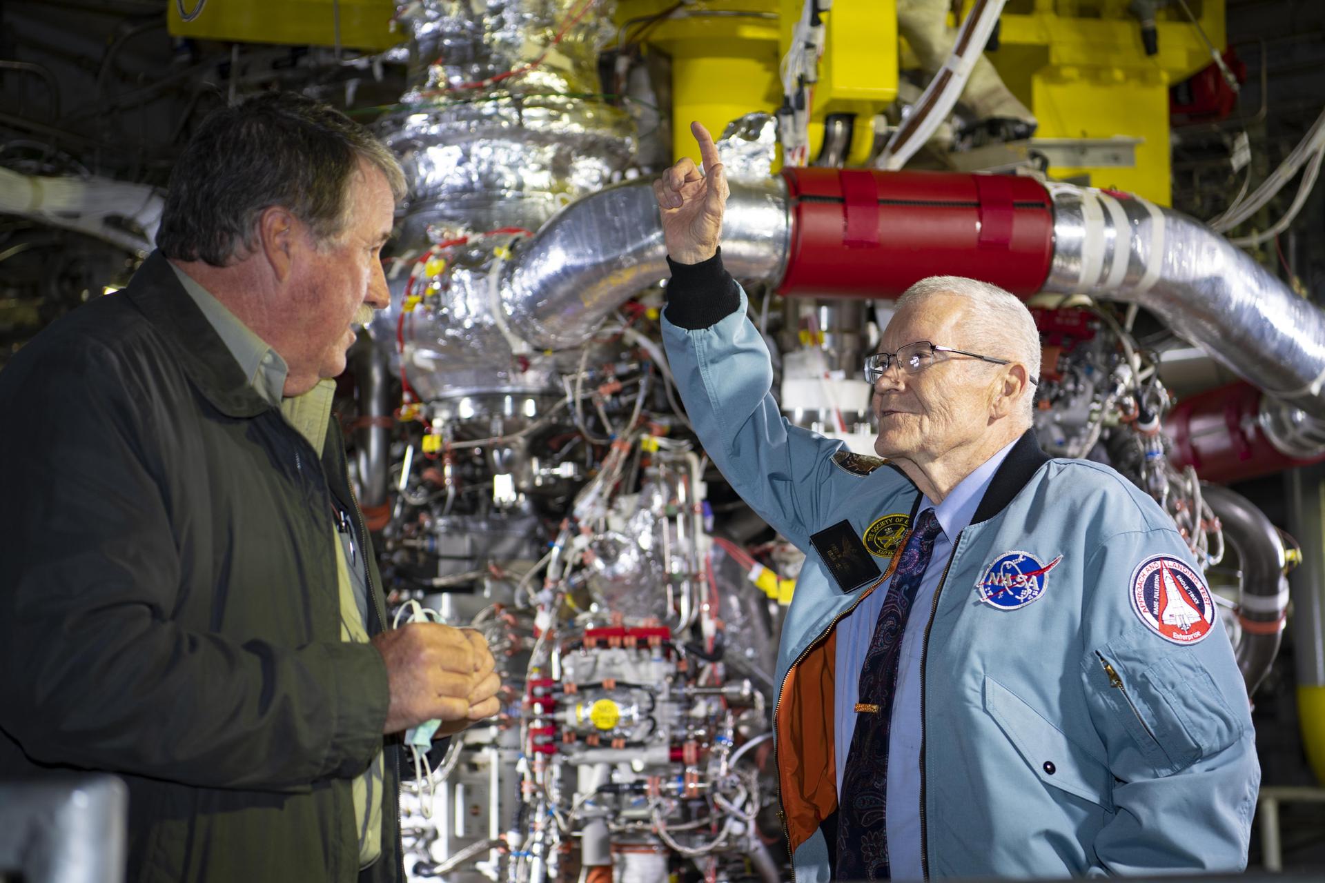 Apollo 13 Astronaut Fred Haise, right, stands in front of an RS-25 rocket engine installed on the A-1 Test Stand along with Jeff Henderson, test director at NASA’s Stennis Space Center