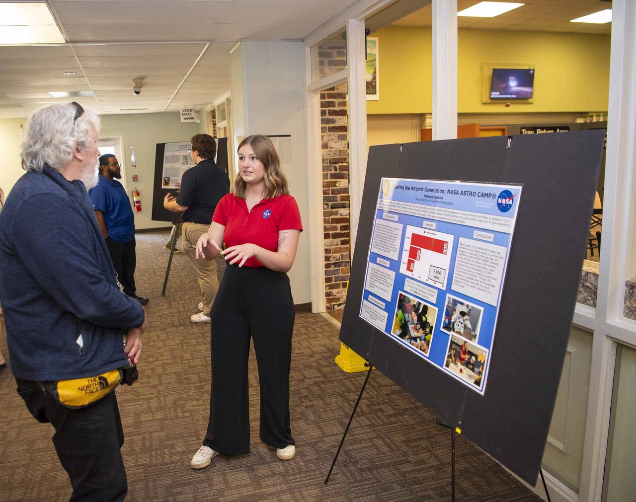 NASA Stennis summer intern Madison Godbold, right, shares about her work of inspiring the Artemis Generation through ASTRO Camp activities during an Aug. 7 event hosted by the Office of STEM Engagement. Godbold, a student at The University of Southern Mississippi in Hattiesburg, worked with the NASA Stennis Office of STEM Engagement. The poster symposium highlighted research topics, including propulsion test operations, lunar robotics, autonomous systems, STEM education, and more. NASA’s Office of STEM Engagement paid internships allow high school and college-level students to contribute to the agency’s mission to advance science, technology, aeronautics, and space exploration.