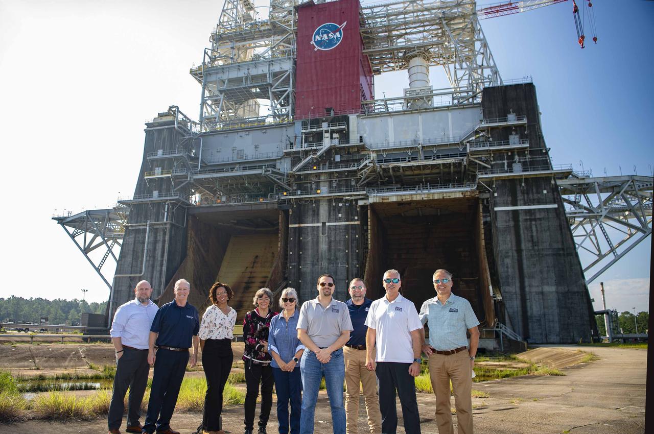 Afognak Native Corporation Board of Director members and Alutiiq, LLC executives stand at the Thad Cochran Test Stand (B-1/B-2) during a visit to NASA’s Stennis Space Center on Sept. 19. The board members and executives visited the site to learn about laboratory services provided by Alutiiq Essential Services at NASA Stennis since 2020. Afognak is an Alaskan corporation focused on serving the needs of its native Alaskan people. Alutiiq, LLC operates as a subsidiary of the corporation to provide a variety of services to federal entities. Alutiiq Essential Services operates as a subsidiary of Alutiiq, LLC. Shown at the test stand during the Sept. 19 visit are, left to right: Ian Neumann, Alutiiq executive; John Monaccio, Alutiiq Essential Services president; Autumn Sellers, Alutiiq executive; Loretta Nelson, director; Marci Orth, director; Wade Hall, director; Shane Mendel, Alutiiq Essential Services program manager at NASA Stennis; Erik Olsen, director; Alan Hines, Alutiiq Essential Services executive.