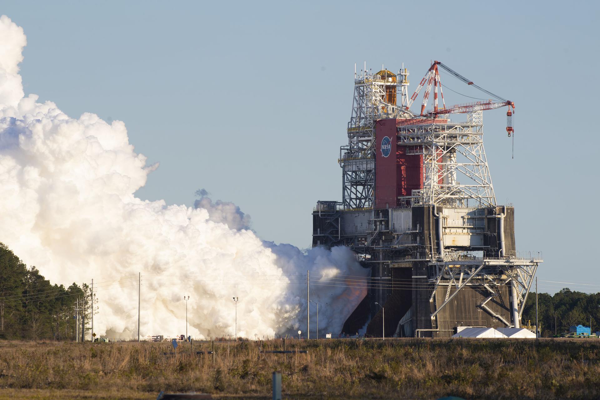 A large liquid-fuelled engine hot-fire test on a vertical test stand, with a plume of white steam.