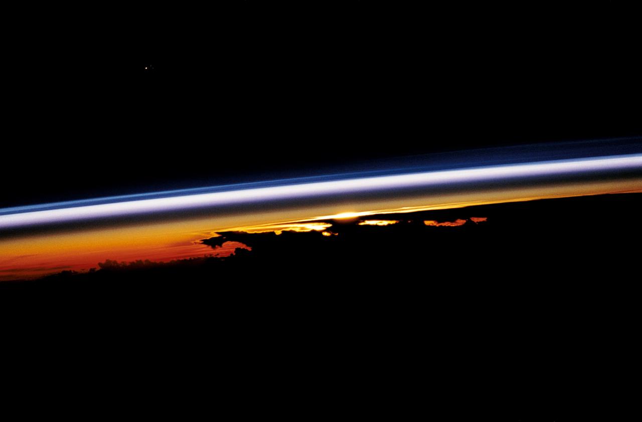STS047-54-018 (12-20 Sept. 1992) --- The colors in this photograph provide insight into the relative density of the atmosphere. The crew members had many opportunities to witness sunrises and sunsets, considering they orbit the Earth every 90 minutes, but few, they said, compared to this scene. It captures the silhouette of several mature thunderstorms with their cirrus anvil tops spreading out against the tropopause (the top of the lowest layer of Earth's atmosphere) at sunset. The lowest layer (troposphere) is the densest and refracts light at the red end of the visible spectrum (7,400 Angstroms), while the blues (4,000 Angstroms) are separated in the least dense portion of the atmosphere (middle and upper atmosphere, or stratosphere and mesosphere). Several layers of blue can be seen. NASA scientists studying the photos believe this stratification to be caused by the scattering of light by particulate trapped in the stratosphere and mesosphere particulate that generally originate from volcanic eruptions, such as those of Mt. Pinatubo in the Philippines and, most recently, Mt. Spurr in Alaska.