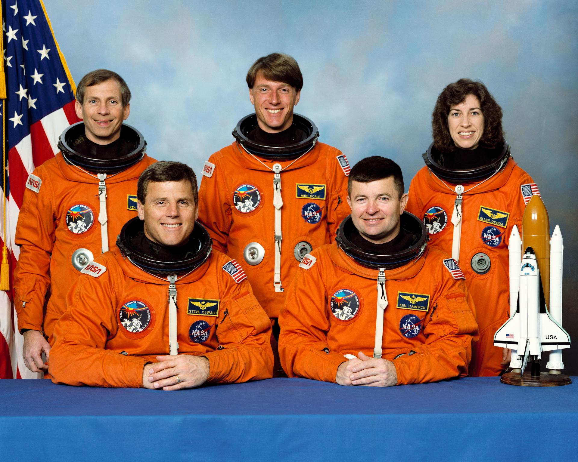 Four men and one woman in orange space suits posing for a crew photo