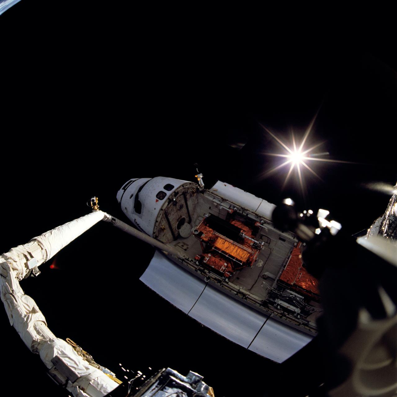 STS061-105-024 (2-13 Dec. 1993) --- One of Endeavour's space walkers captured this view of Endeavour backdropped against the blackness of space, with the Sun displaying a rayed effect. The extended Remote Manipulator System (RMS) arm that the astronaut was standing on is seen on the left side of the view.