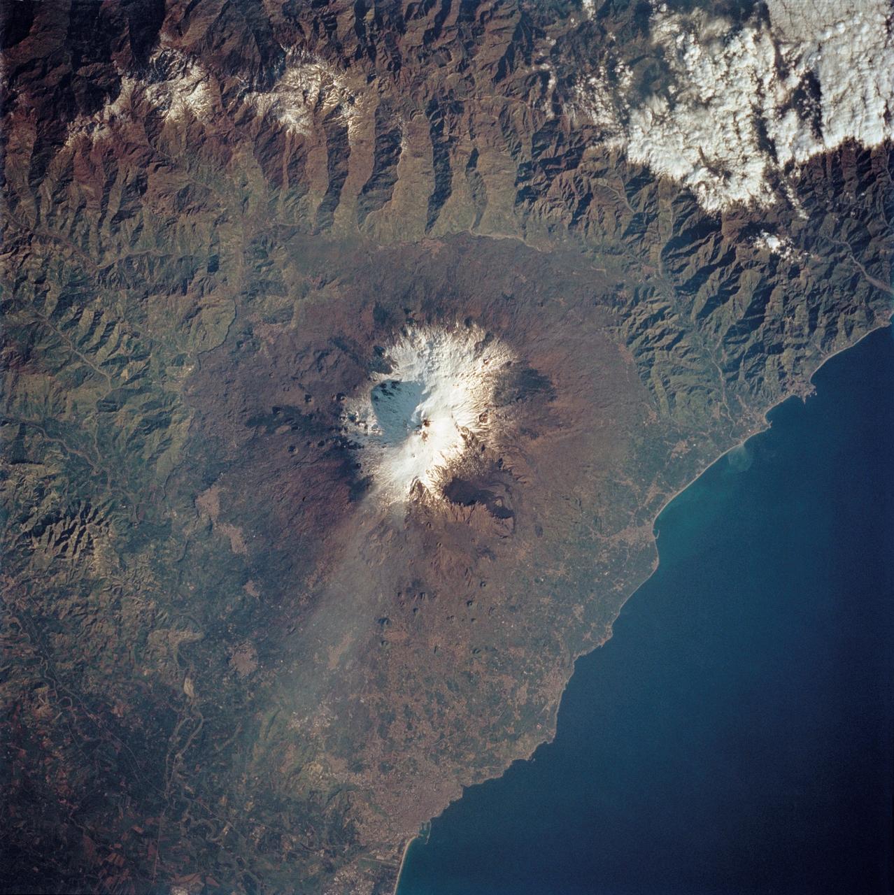 STS062-85-195 (4-18 March 1994) --- A thin plume of steam blows southward from the summit of Mt. Etna, the active volcano on the island of Sicily. The summit is capped with snow but the dark lava flow along the eastern flank (the 1991-93 flow) is clearly visible. The coastal city south of Etna is Catania.