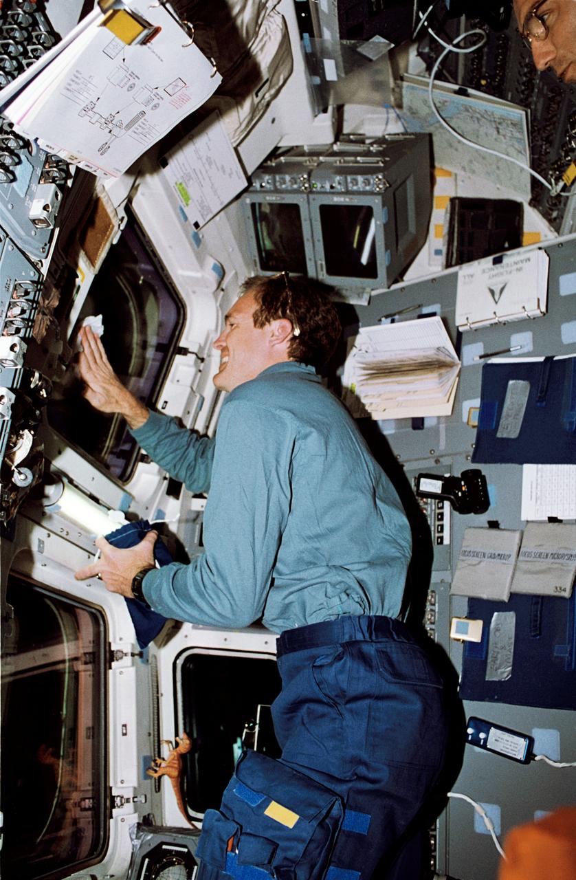 STS065-52-034 (8-23 July 1994) --- On the Space Shuttle Columbia's aft flight deck, astronaut James D. Halsel,l Jr., pilot, cleans off one of the overhead windows. Astronaut Carl E. Walz, mission specialist, looks on (photo's edge). The two shared over fourteen days in Earth-orbit with four other NASA astronauts and a Japanese payload specialist in support of the second International Microgravity Laboratory (IML-2) mission.