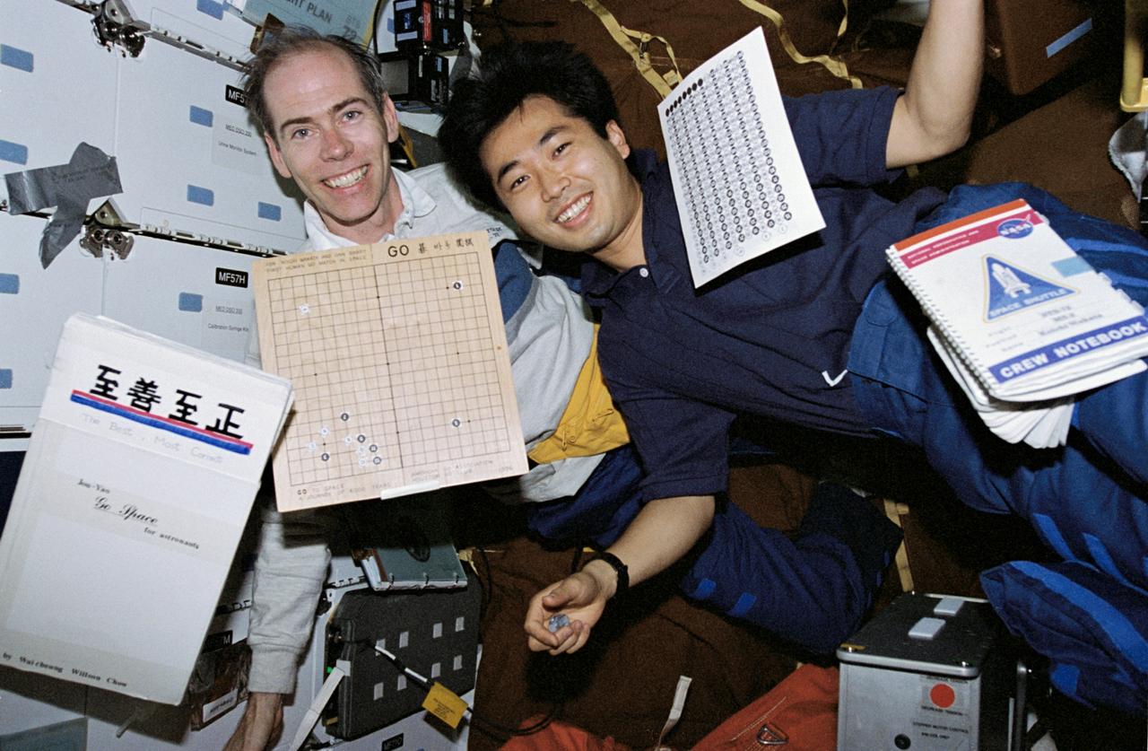 STS072-315-034 (11-20 Jan. 1996) --- During off-duty time aboard the Space Shuttle Endeavour, astronauts Daniel T. Barry (left) and Koichi Wakata join on the middeck for an in-space version of a Japanese game called "Go". Because of microgravity, the usual rock-like pieces that are moved about on the board by each player had to give way to tiny stick-on pieces. Wakata represents Japan's National Space Development Agency (NASDA).