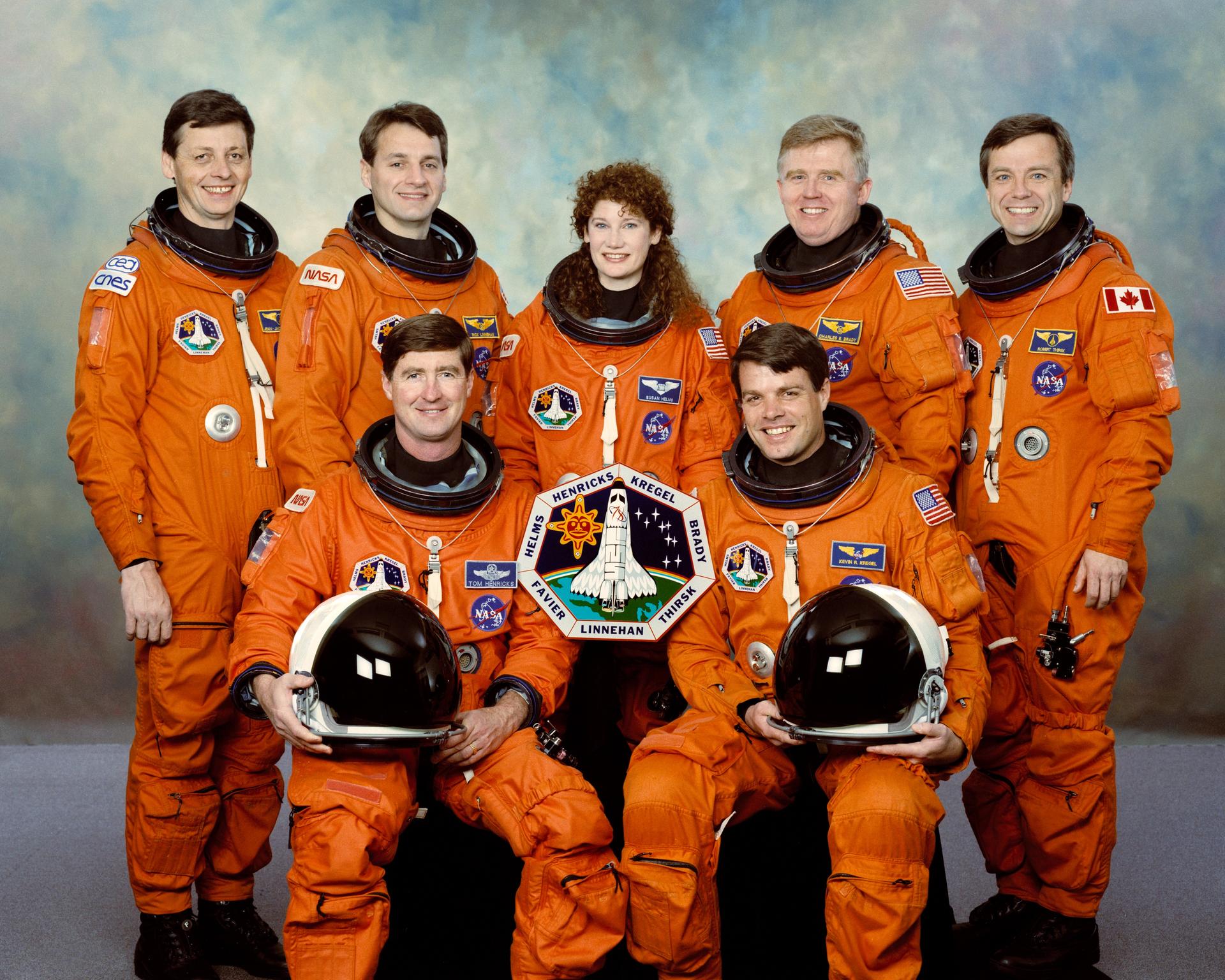 Seven astronauts in orange spacesuits pose for crew photo.