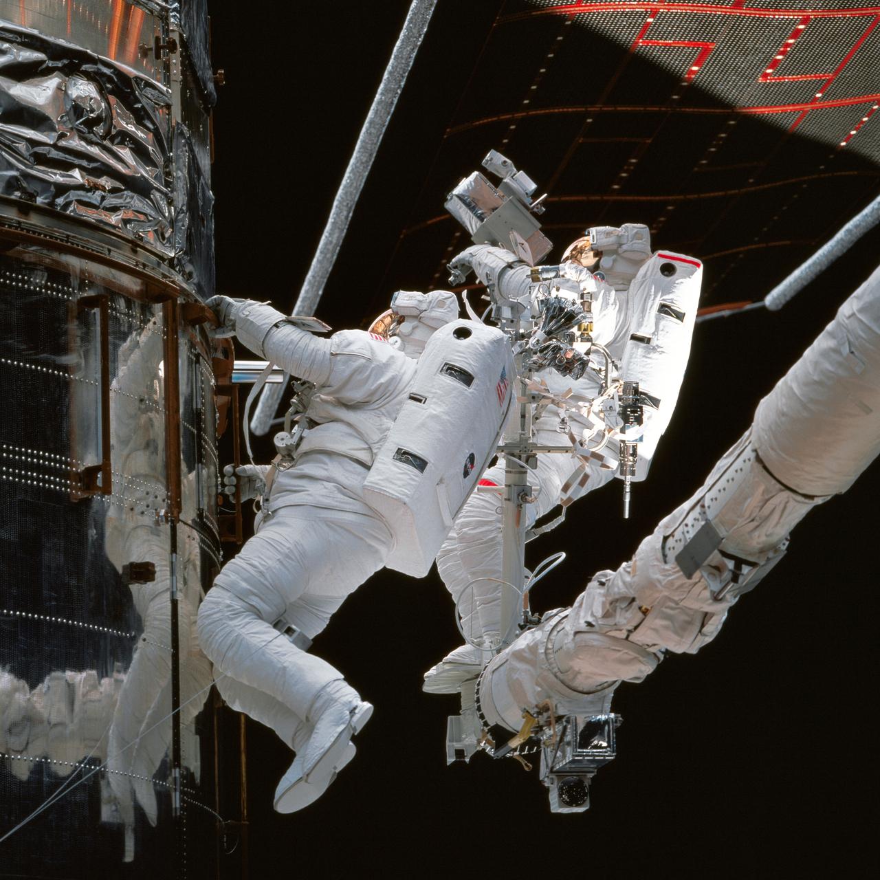 STS082-738-054 (11-21 Feb. 1997) --- As photographed from inside the Space Shuttle Discovery?s crew cabin, astronauts Steven L. Smith (left) and Mark C. Lee (red stripe) inspect insulation around Bay 10 of the Hubble Space Telescope (HST) during one of five days of extravehicular activities (EVA) designed to service the HST.  Lee, payload commander, and Smith, performed three of the five EVA?s which eventually were carried out on the mission.