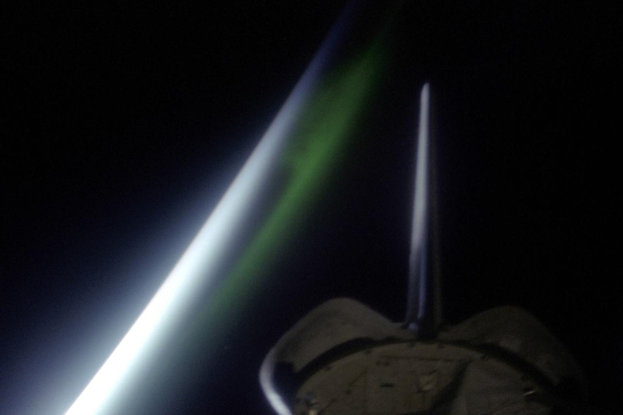 STS099-349-002 (11-22 February 2000) ---The Space Shuttle Endeavour's vertical stabilizer is visible in the foreground of this 35mm frame featuring airglow, the thin greenish band above the horizon. Airglow is radiation emitted by the atmosphere from a layer about 30 kilometers thick and about 100 kilometers altitude. The predominant emission in airglow is the green 5577-Angstrom wavelength emission from atomic oxygen atoms. Airglow is always and everywhere present in the atmosphere; it results from the recombination of molecules that have been broken apart by solar radiation during the day. But airglow is so faint that it can only be seen at night by looking "edge on" at the emission layer, such as the view astronauts have in orbit.
