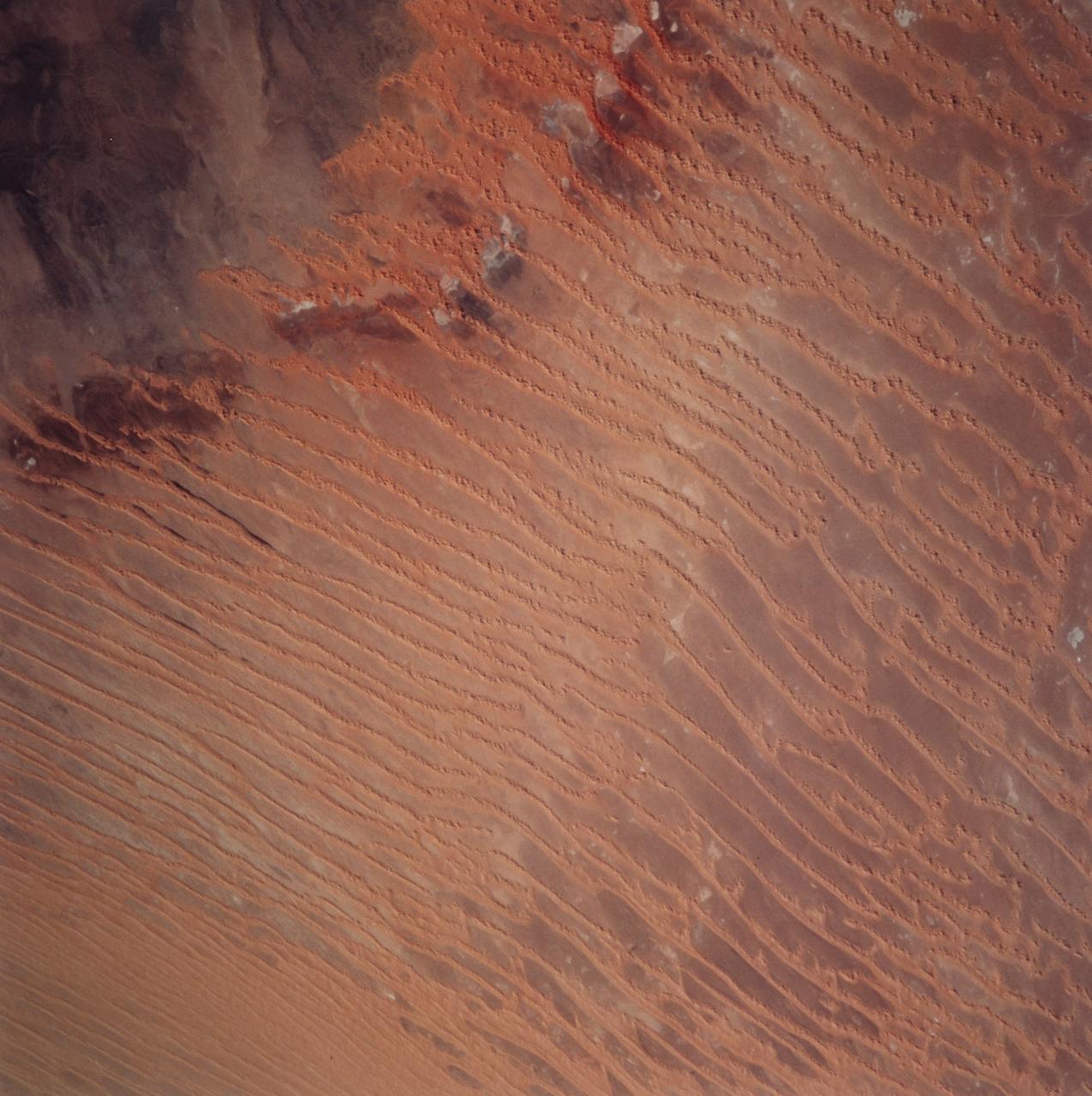 STS099-729-045 (11-22 February 2000) ---This Earth scene from the Space Shuttle Endeavour features linear dunes in the Algerian Saharan sand sea known as the Erg Chech.  The dunes, according to NASA scientists, have been built up over thousands of years into masses elongated roughly parallel with the prevailing northeast winds.  Dune chains in the northern (upper) half of the view are 5-8 kilometers apart.  A slight change in orientation and an increase in the density of dunes appear across the middle of the view.  Such changes usually relate to changes in sand supply, and also to topographic scarps over which the dunes pass.  Obstacles like scarps and hills locally cause a leftward deflection (in the Northern Hemisphere) in wind direction, an effect that can be seen here in the dune orientation in the middle of the photo.  Dunes in the lower part of the view are 2-5 kilometers apart.  White patches are small dry lakes at low points in the underlying rock surface.  The strong red color in some dunes near the edge of the dune field (left margin) is iron staining derived from sand particles blown into the dunes from the underlying iron-rich soils.  A dune-free area appears in the lower left corner.