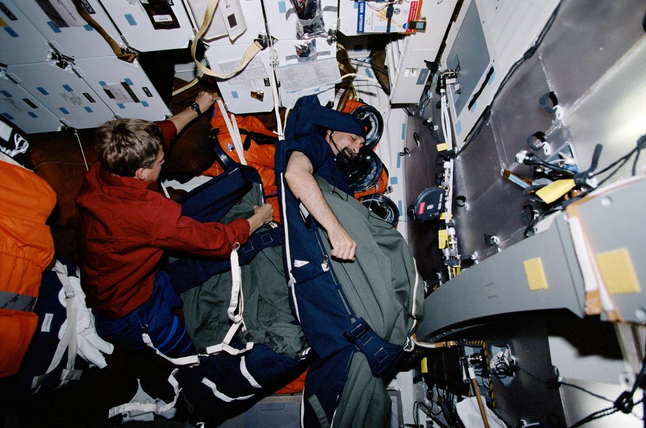 STS100-363-012 (19 April-1 May 2001) --- Astronaut Umberto Guidoni, STS-100 mission specialist, sleeps while astronaut Scott E. Parazynski, mission specialist, prepares for his sleep shift on the Space Shuttle Endeavour's middeck.